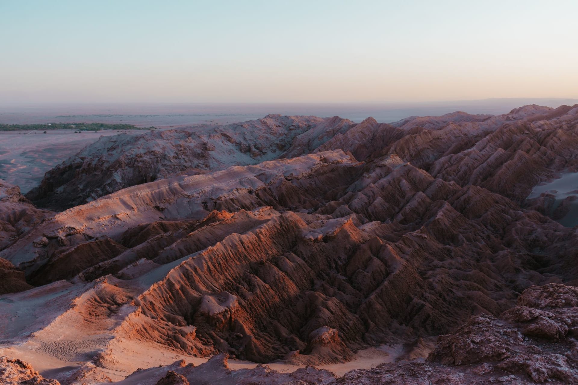 A lone figure standing at the crest of a terracotta-red sand dune in Valle de la Muerte with jagged dark rock formations below