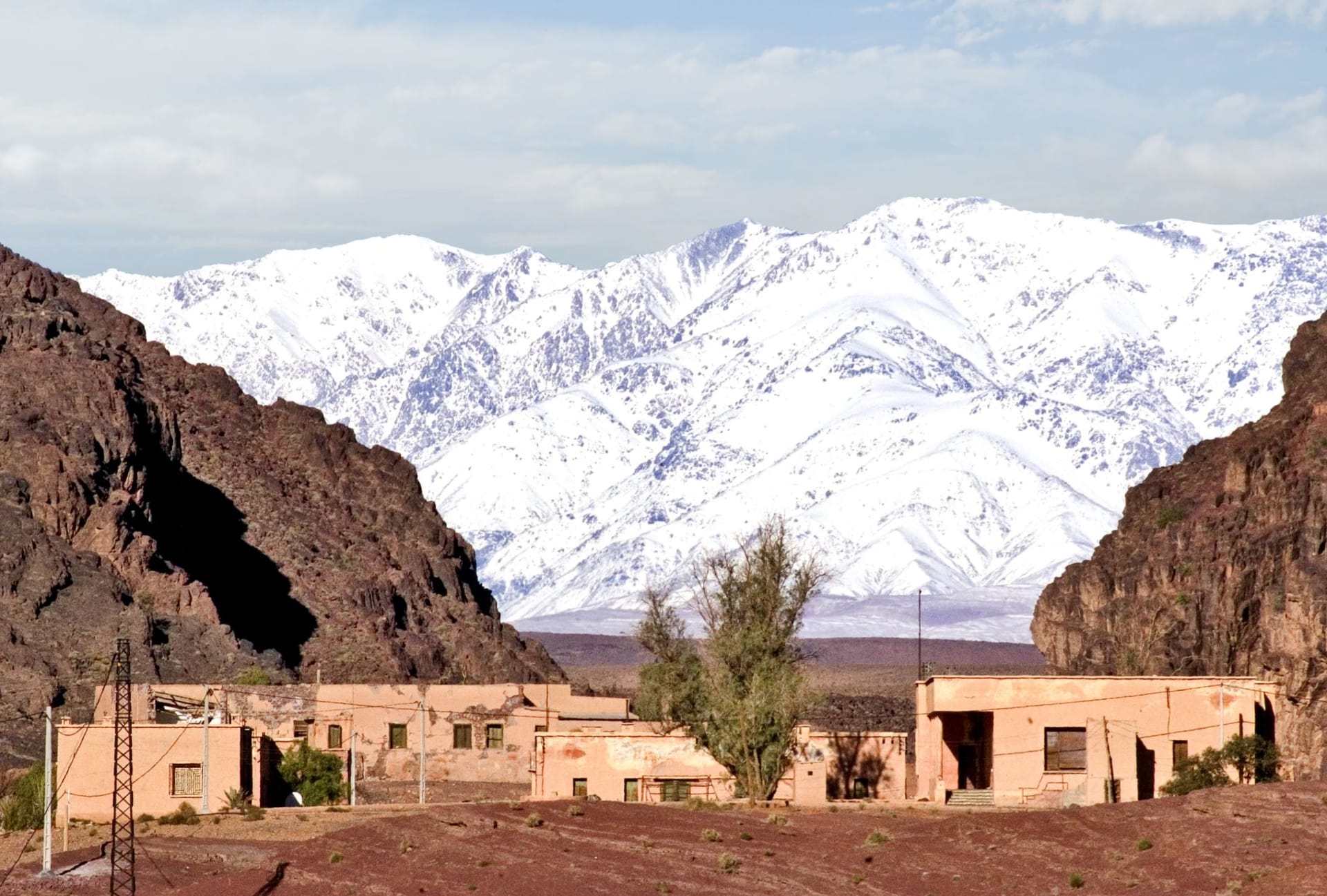 Taourirt Kasbah in Ouarzazate glowing amber at dusk, palm trees and the pre-Saharan plain stretching beyond