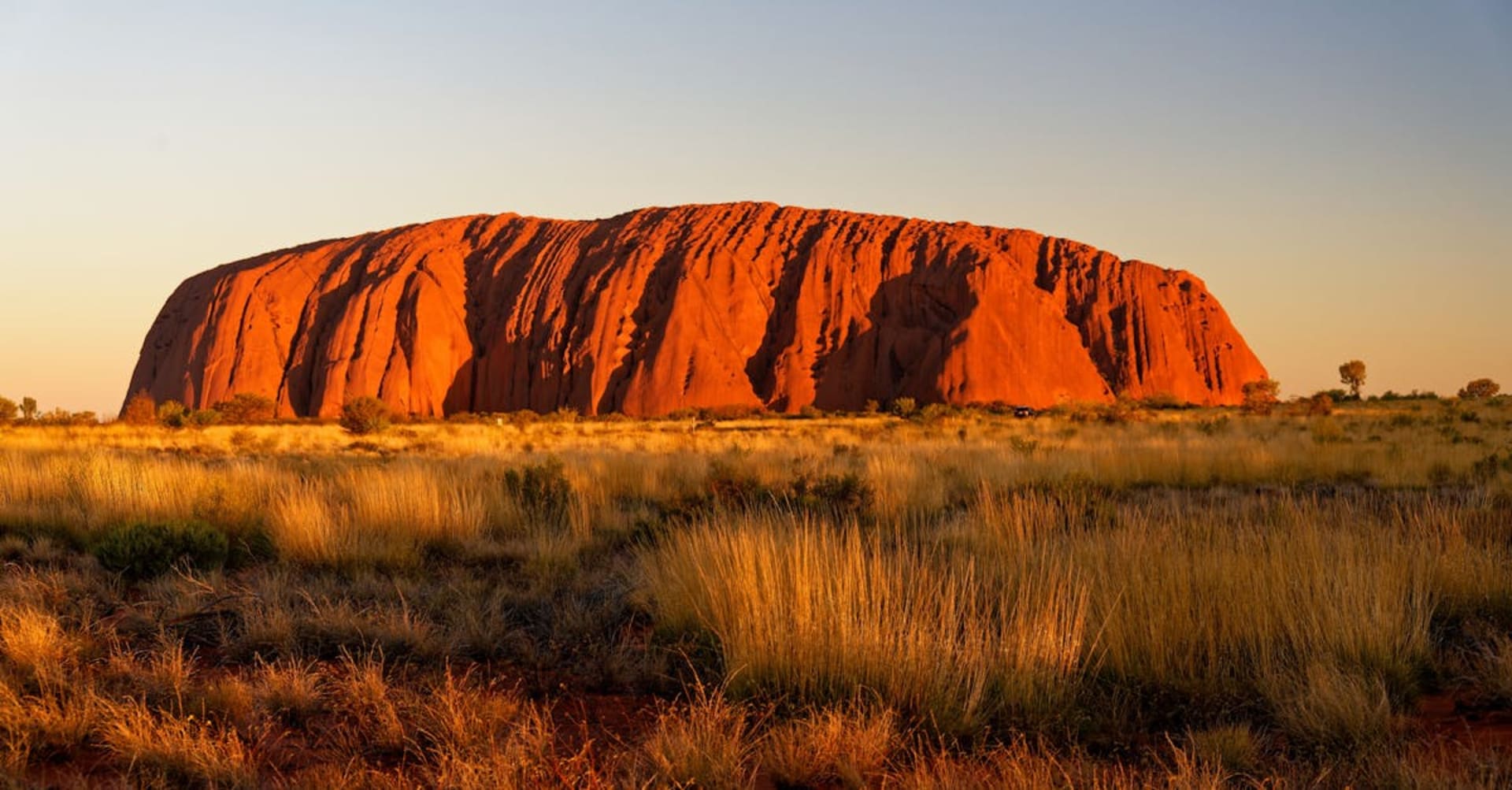 Uluru monolith glowing red at sunset against a vast desert sky