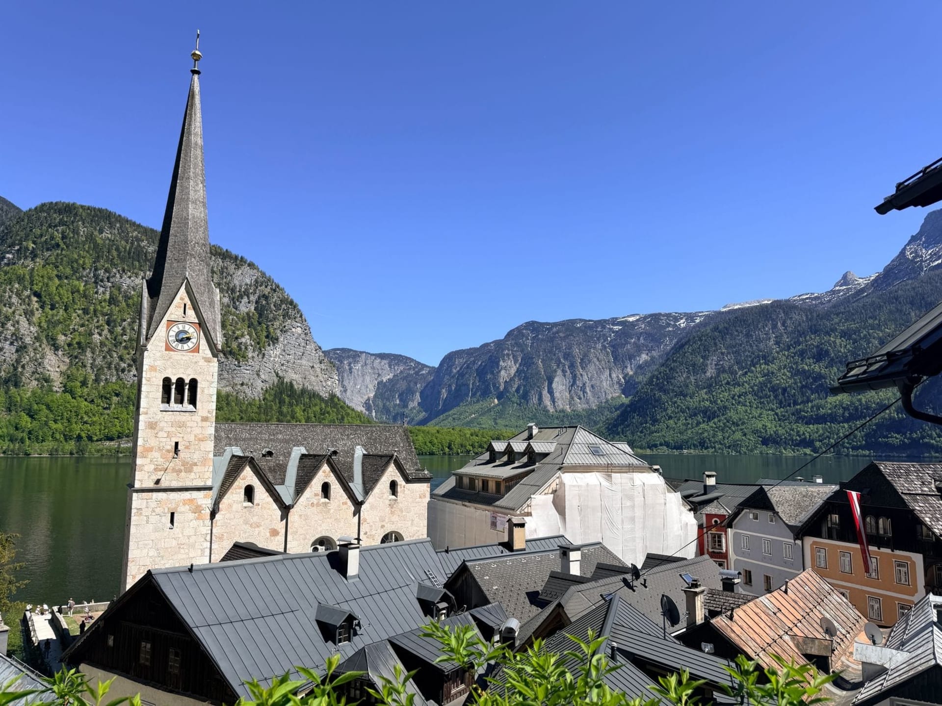 Hallstatt village reflected in the still waters of Hallstätter See, with white-painted houses stacked against a steep limestone cliff and a church spire rising above the treeline