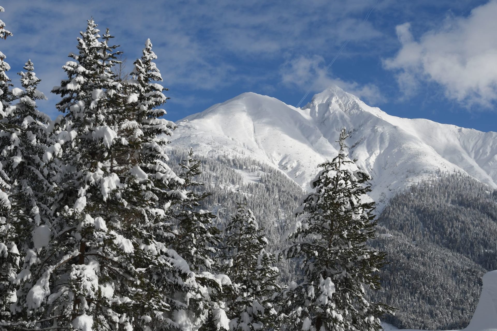 Seefeld in Tirol village in winter with the Seekirchl chapel on its hilltop, fresh snow on the pine forests surrounding the plateau and the Wetterstein mountains behind in blue sky