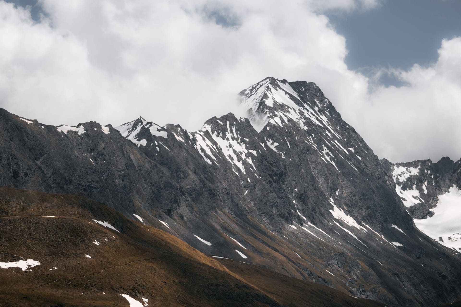 The Stubai Glacier in summer with skiers on the snowfield and the rocky Schaufelspitze peak rising behind, the Stubaital valley visible far below under blue sky