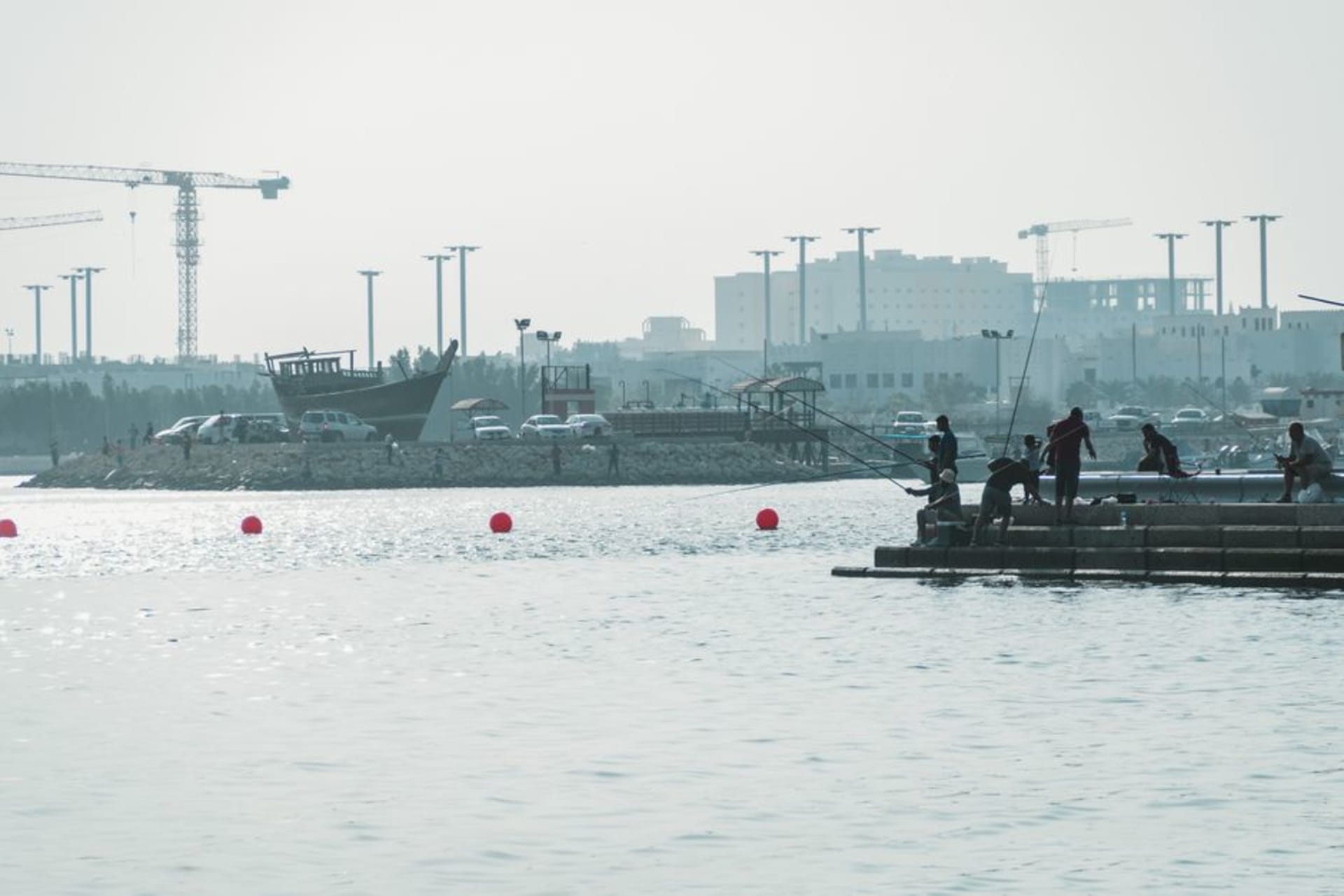 Barcos de pesca amarrados a lo largo de un muelle en Sitra con torres de refinería visibles entre la neblina a lo lejos
