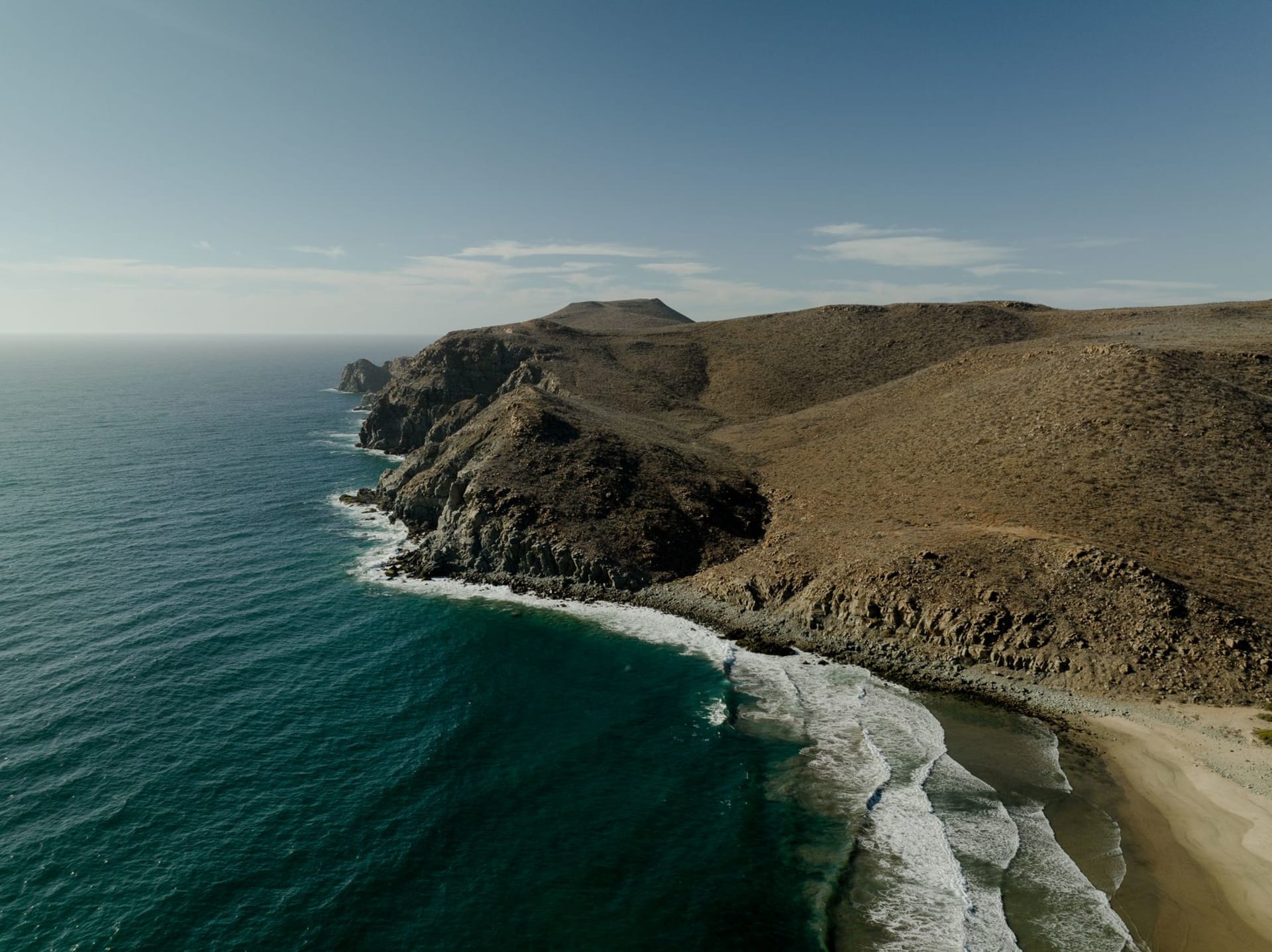 The Mulegé river winding through a dense grove of date palms toward the Sea of Cortez, with the arid Baja hills rising on either side and a small mission church visible on the hill