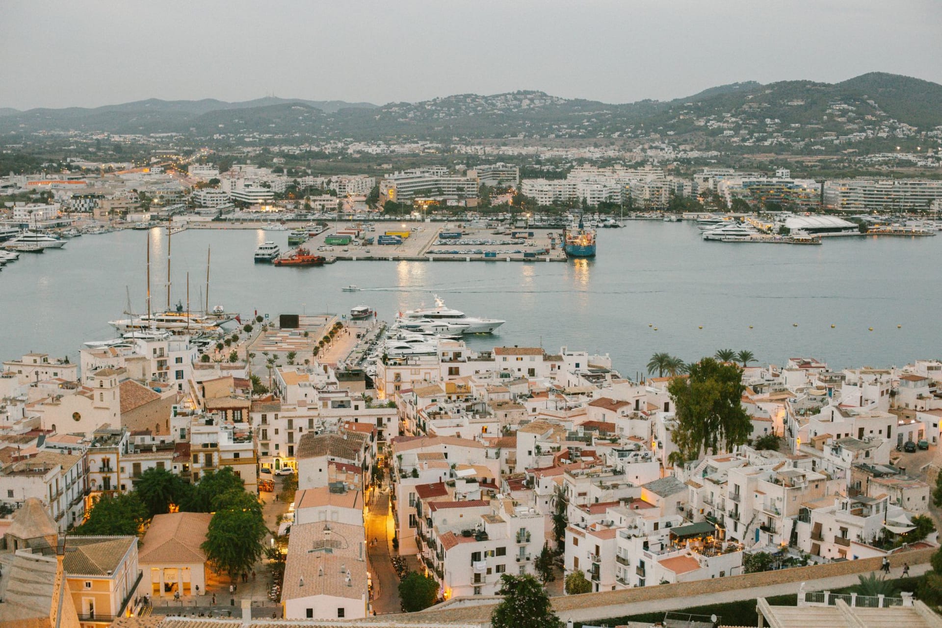 Dalt Vila's ramparts and cathedral tower rising above Ibiza harbor at dusk, warm stone against purple sky
