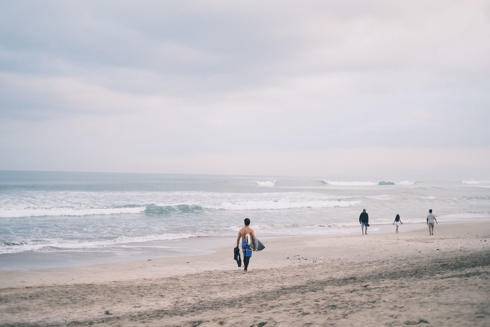 Surfers at Echo Beach in Canggu at golden hour, dark volcanic sand and warm evening light on the breaking waves