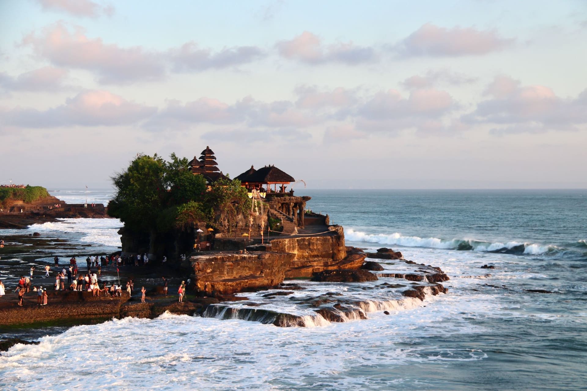 Pura Tanah Lot sea temple silhouetted against a blazing sunset sky, waves breaking around the black rock base