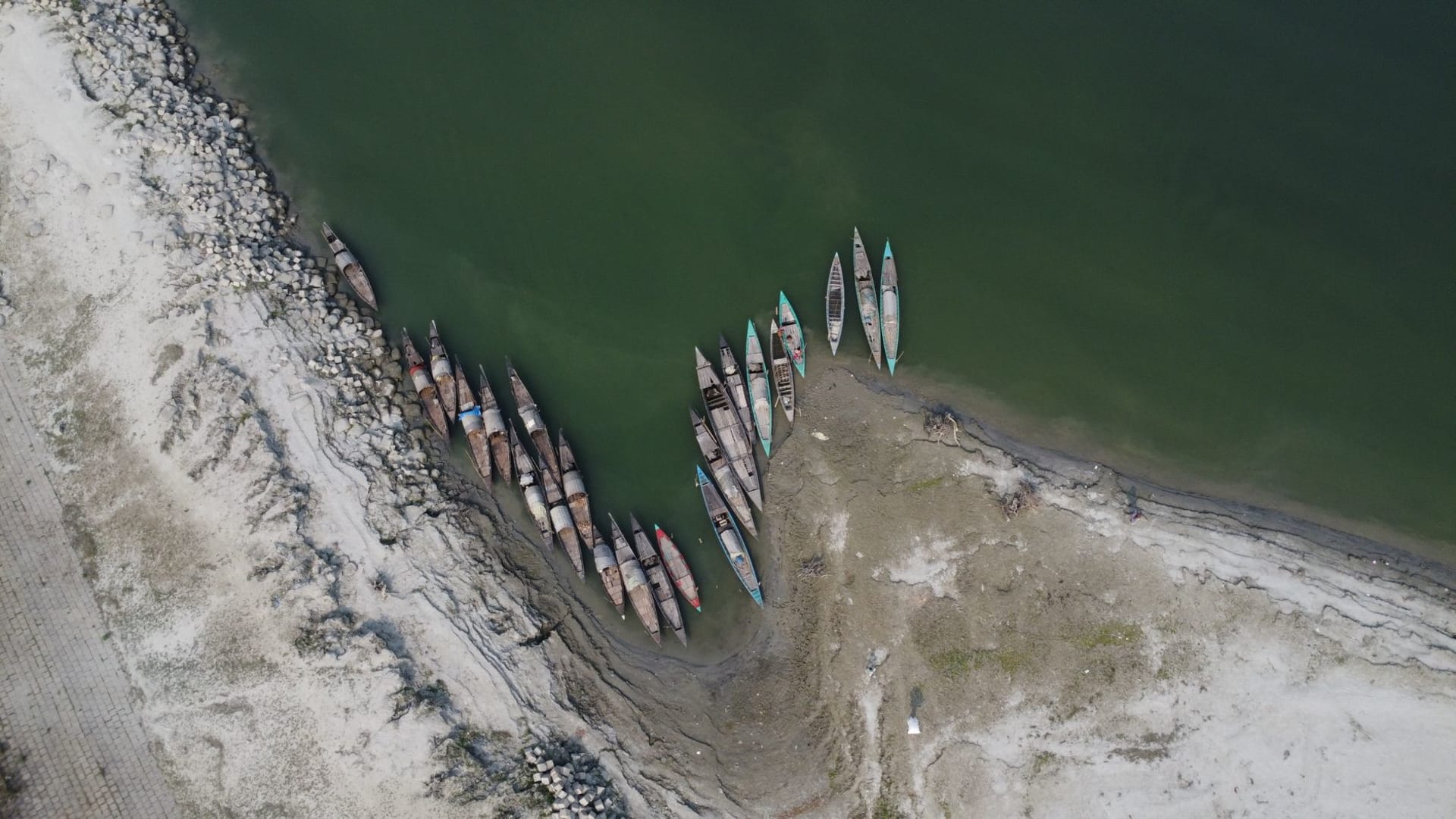 Vista aérea de barcas de madera amarradas a la orilla arenosa de un río en Bangladés, con la serena belleza natural del paisaje del delta