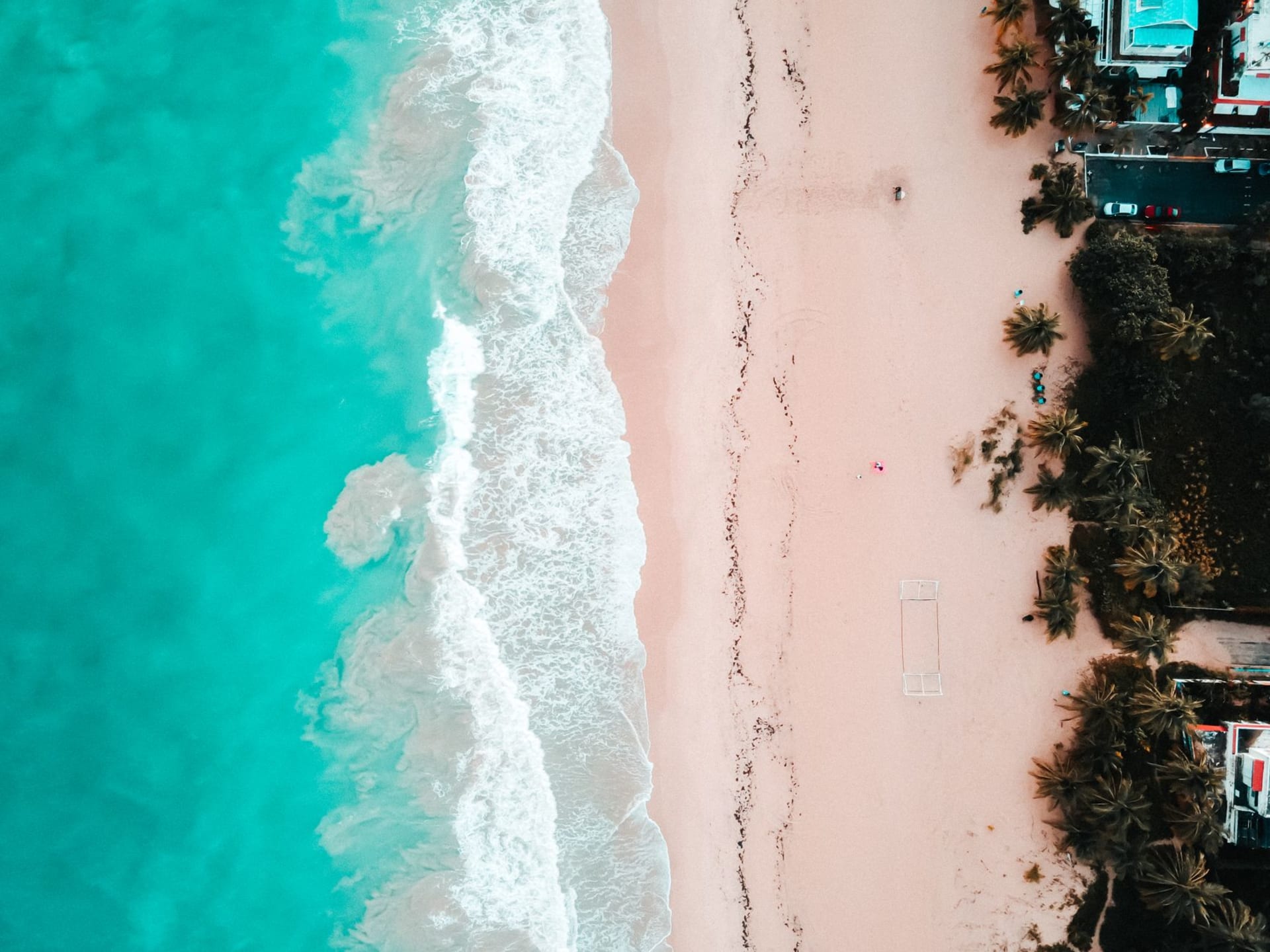 Pink-tinged sand and turquoise breaking waves at Crane Beach with the cliff and historic hotel above