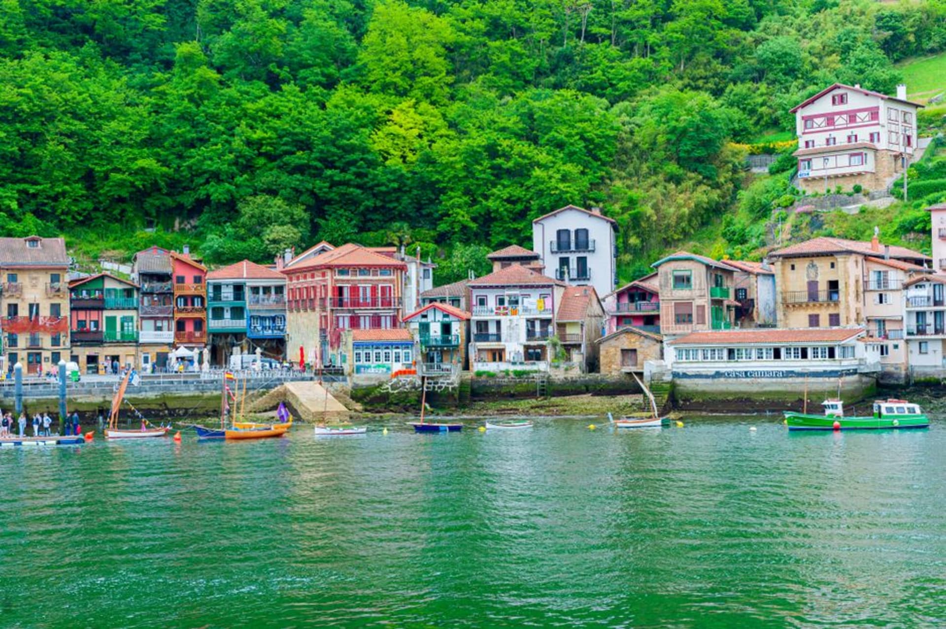 Coloridos barcos de pesca amarrados a lo largo del estrecho canal de Pasaia con altas casas frente al mar reflejadas en el agua
