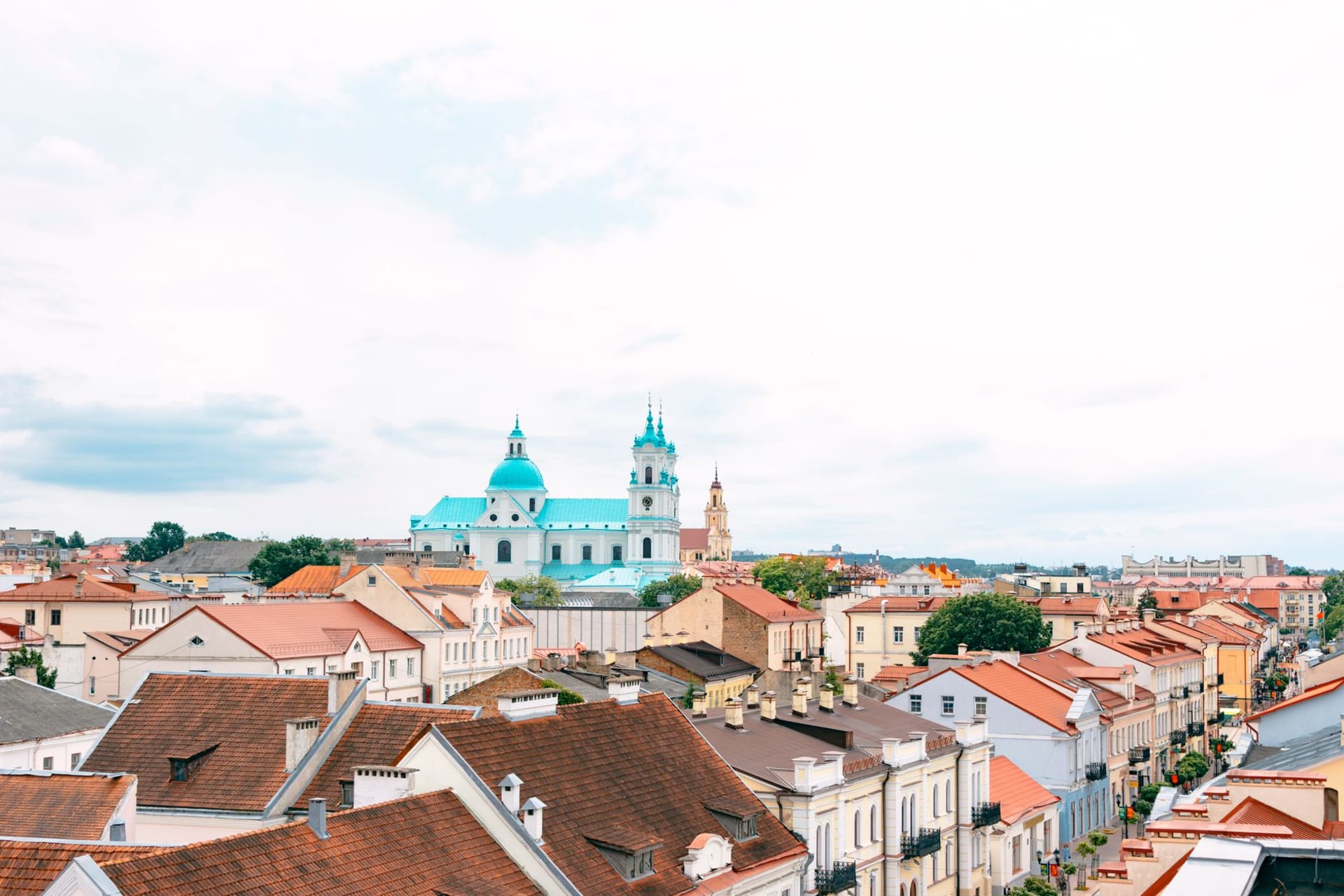The multi-spired skyline of Grodno old town at sunset, with the Neman River curving below and Baroque churches rising above the hill in warm light
