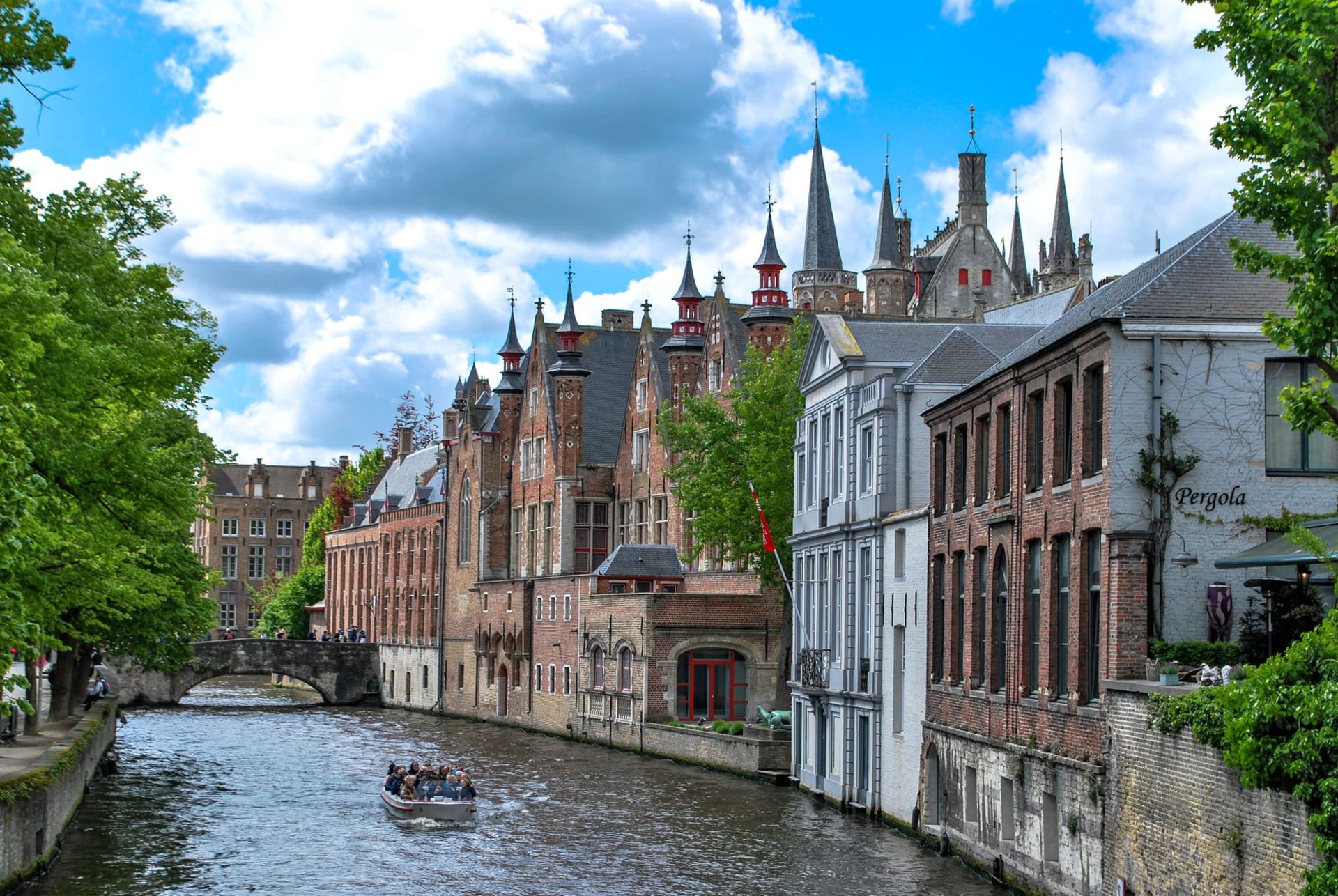 Charming canal scene in Bruges with historic stepped-gable facades and a tour boat on a sunny day