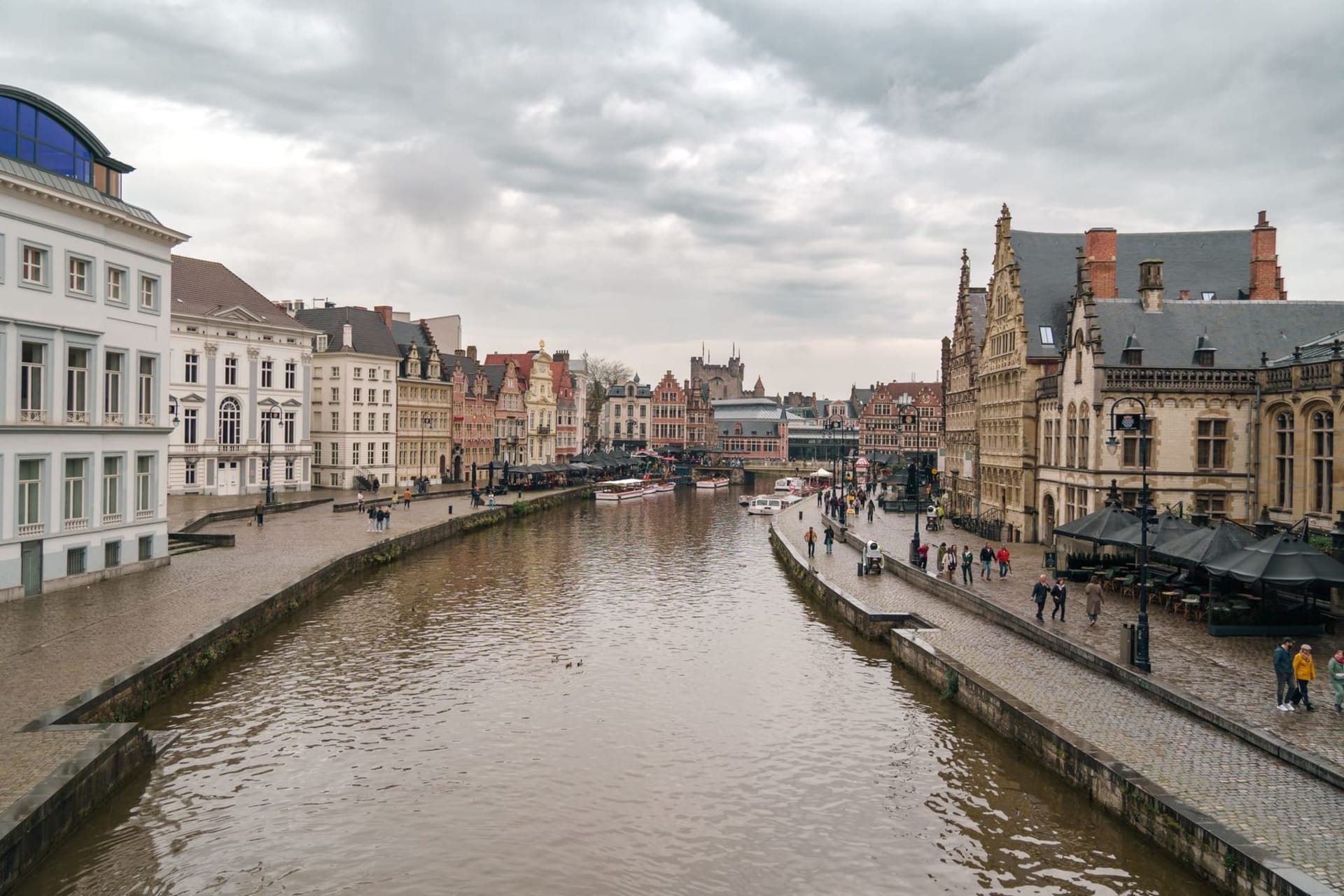 The Graslei canal at dusk, with guild houses reflected in still water and the spires of Saint Nicholas Church and the Belfry rising behind them against a pale evening sky.