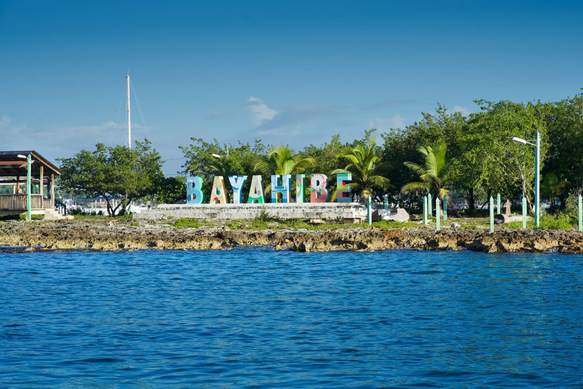 Colorful wooden buildings along a sandy path on Caye Caulker, turquoise sea visible between the palms