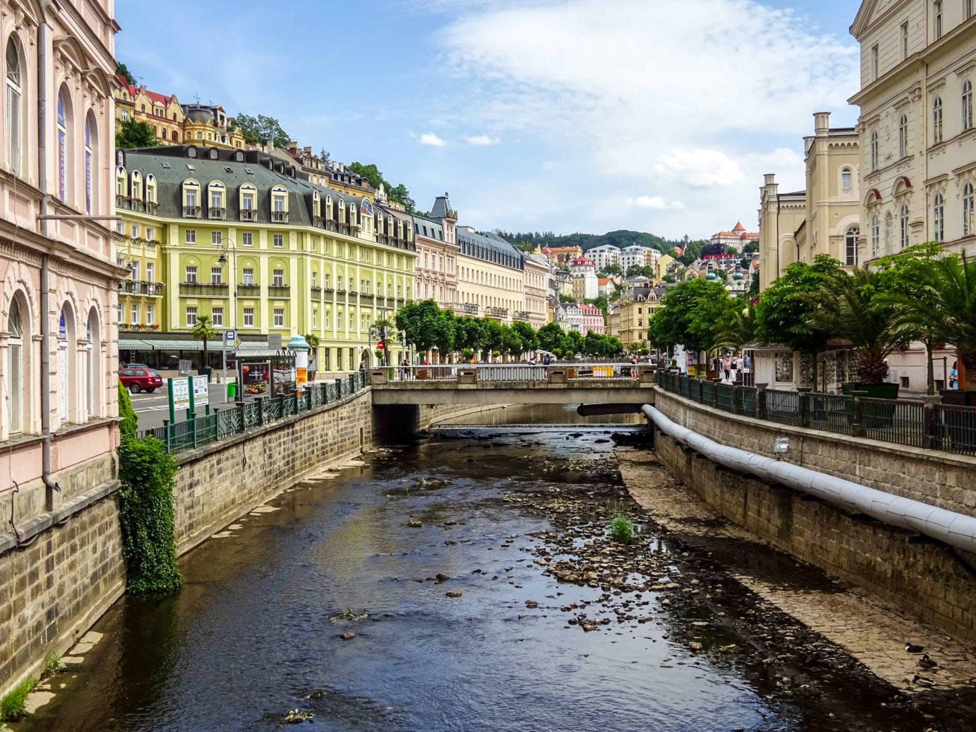 The neoclassical Mill Colonnade stretching along the Teplá River gorge in Karlovy Vary, with steam rising from mineral springs on a cool morning