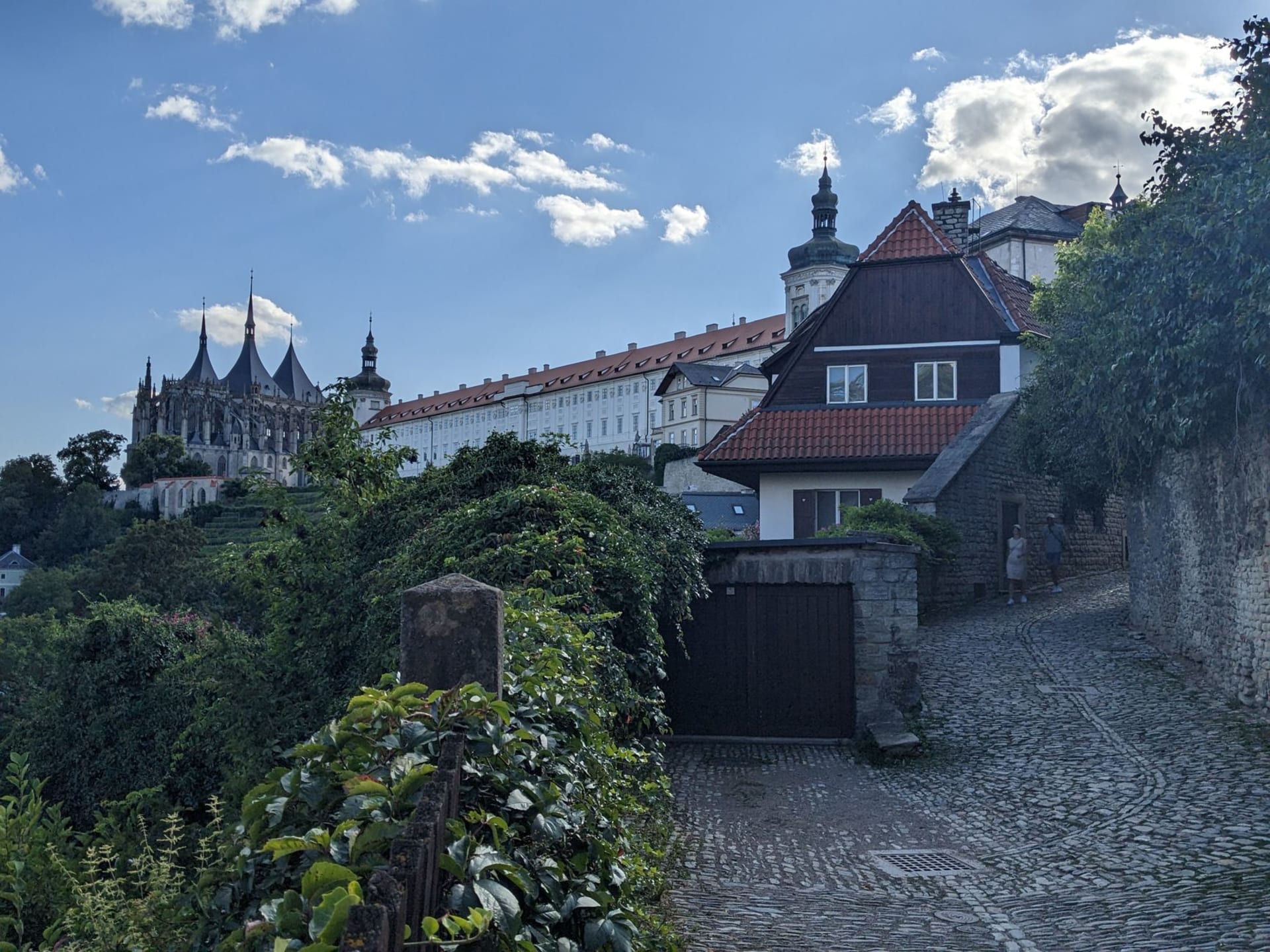 Loket Castle perched on its granite promontory above the Ohře River gorge, the river making a tight loop around the medieval village below, photographed from the forested hillside opposite
