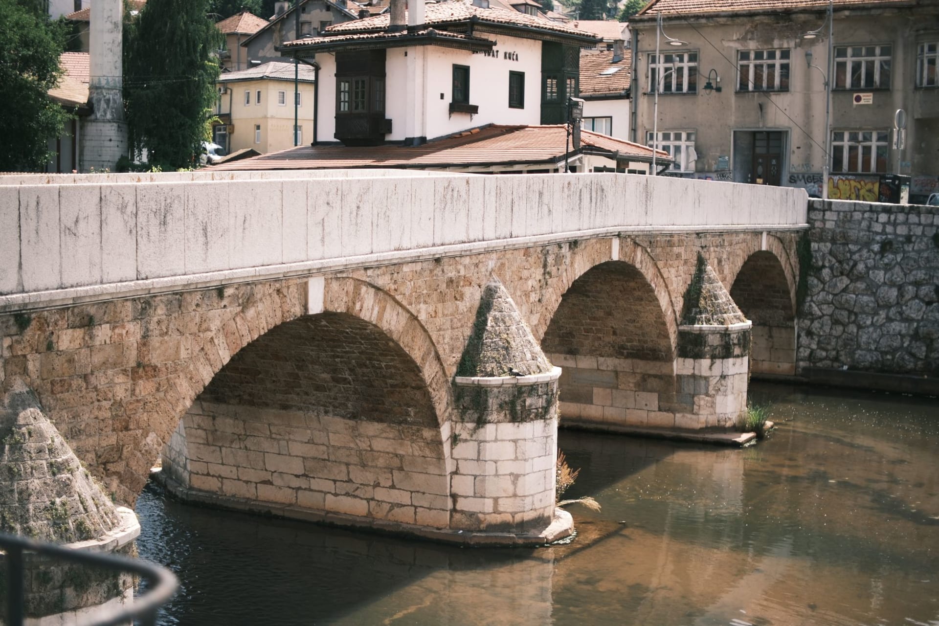 The eleven stone arches of the Mehmed Paša Sokolović Bridge spanning the emerald Drina river at Višegrad, hills rising behind