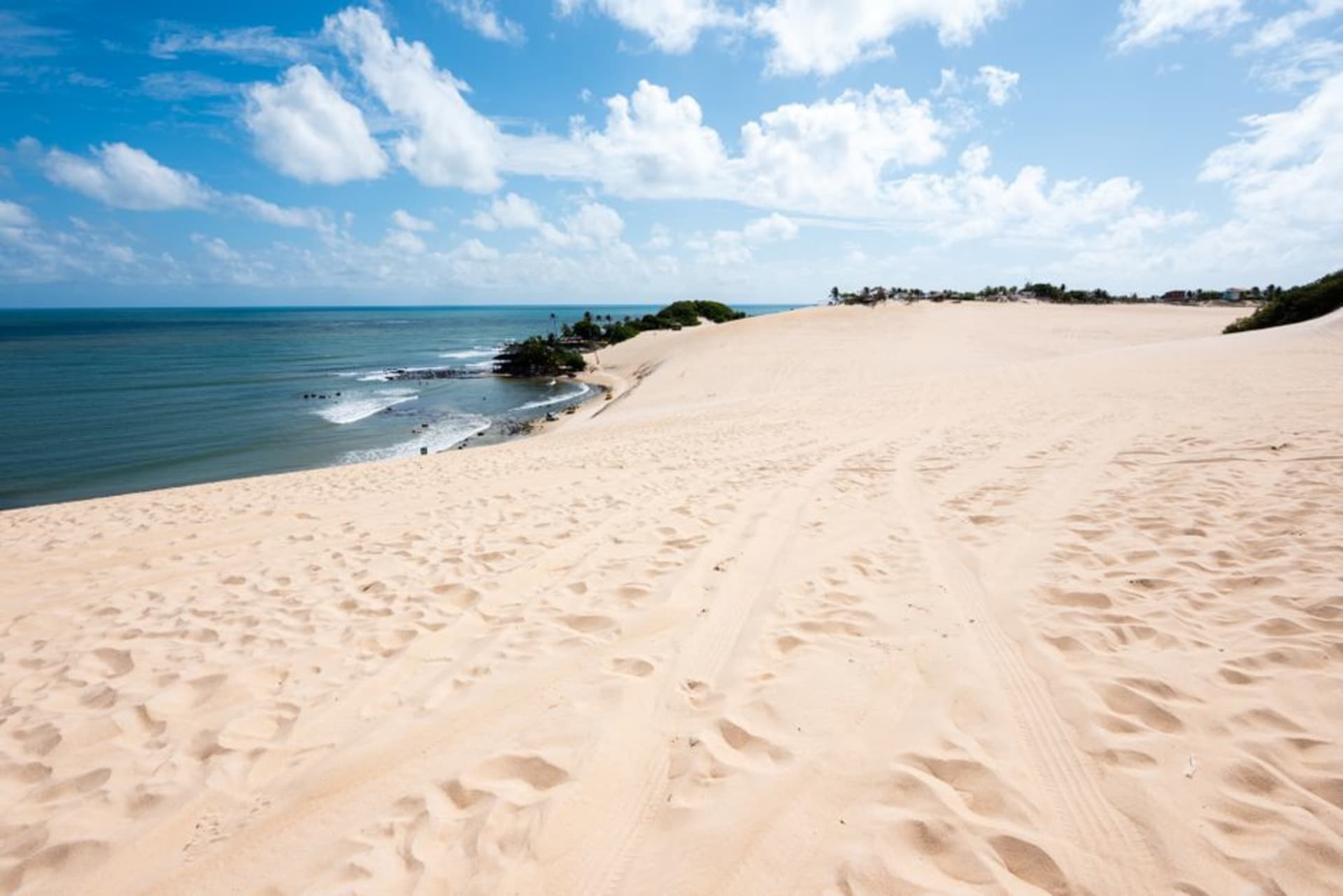 A dune buggy cresting a tall golden sand dune at Genipabu with the Atlantic ocean visible in the distance
