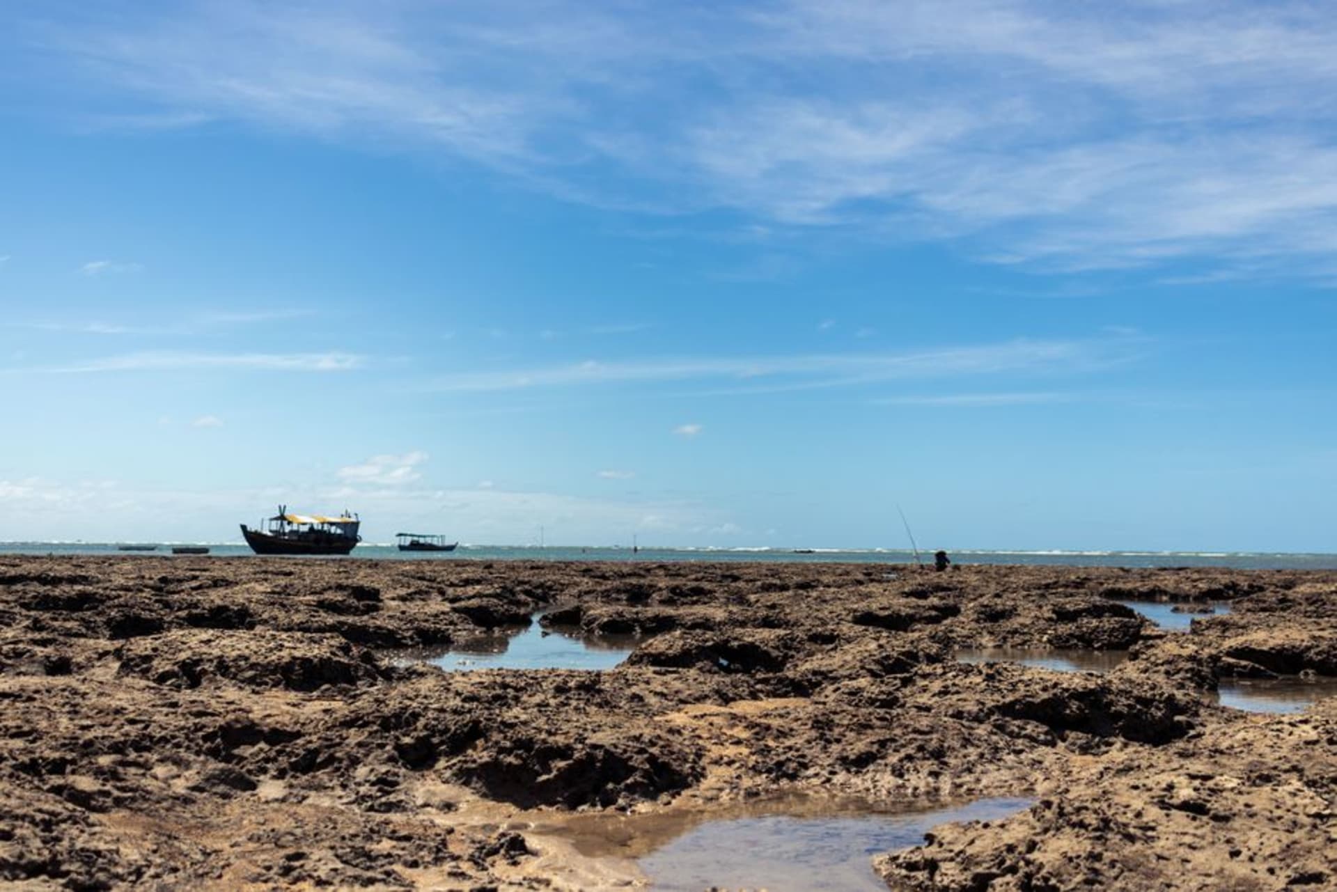 Multicolored sandstone cliffs and eroded formations at Morro Branco beach, streaked in red, ochre, and white bands, with the Atlantic visible at the base