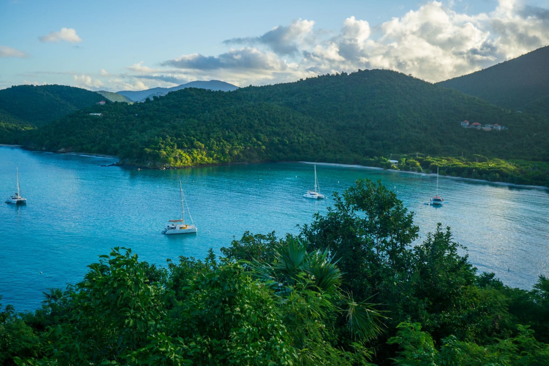 Great Harbour on Jost Van Dyke with colorful wooden beach bars backed by green hills and sailboats anchored in the calm bay