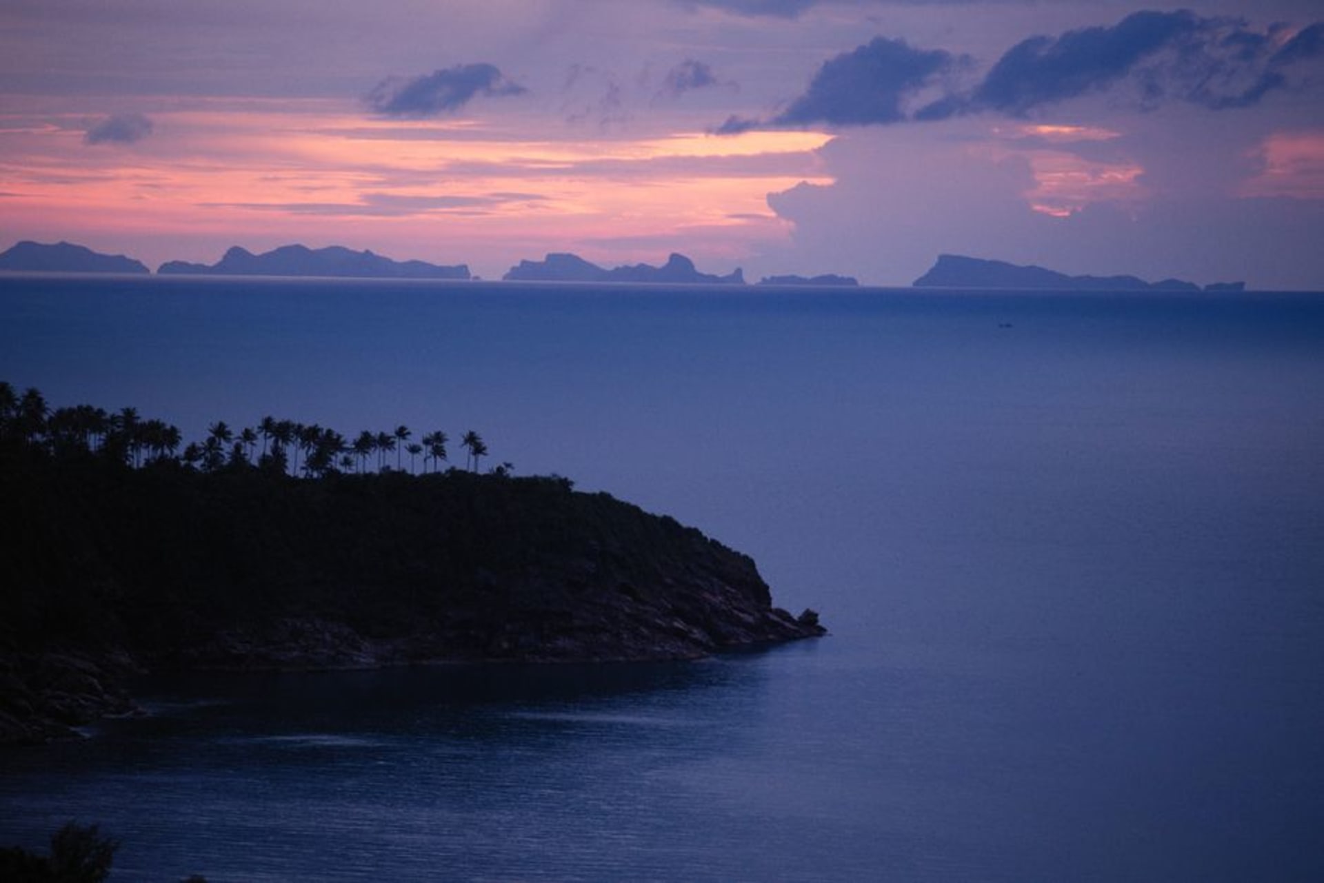 Trellis Bay al atardecer en Beef Island con barcos anclados, una playa de arena bordeada de pequeñas tiendas y agua en calma reflejando el cielo nocturno