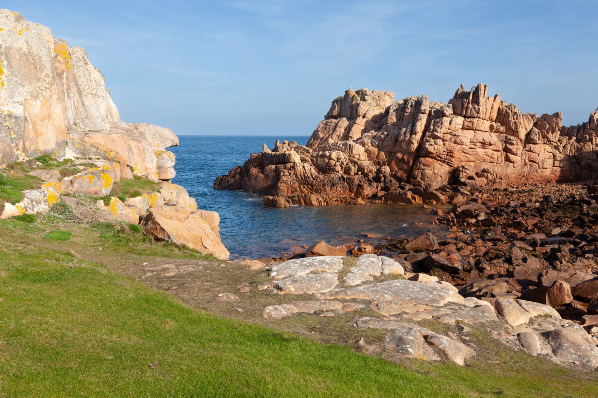 Pink granite rocks and wild coastal heathland on Île de Bréhat, Brittany, at low tide with turquoise water