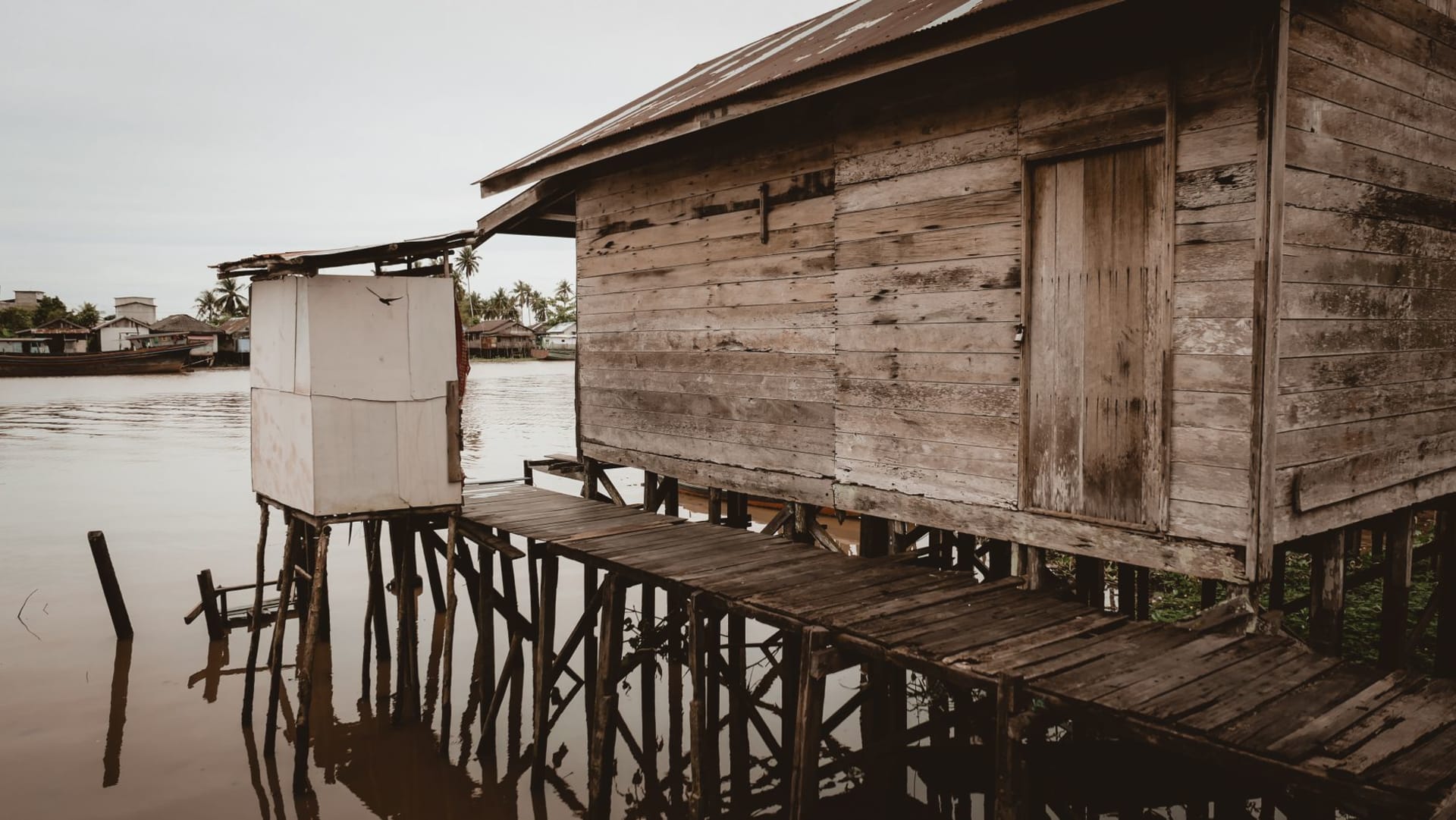 Aerial view of Kampong Ayer's dense wooden houses on stilts over the Brunei River, with the golden mosque dome visible in the background