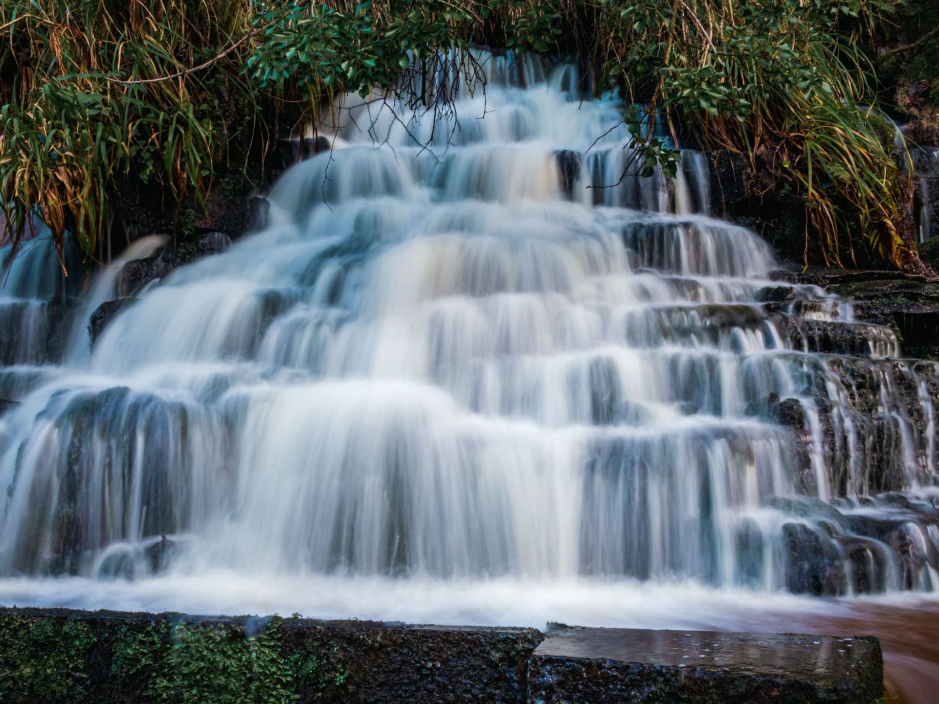 The main Karera waterfall plunging into a dark canyon gorge, white water and mist rising against dense green rainforest walls