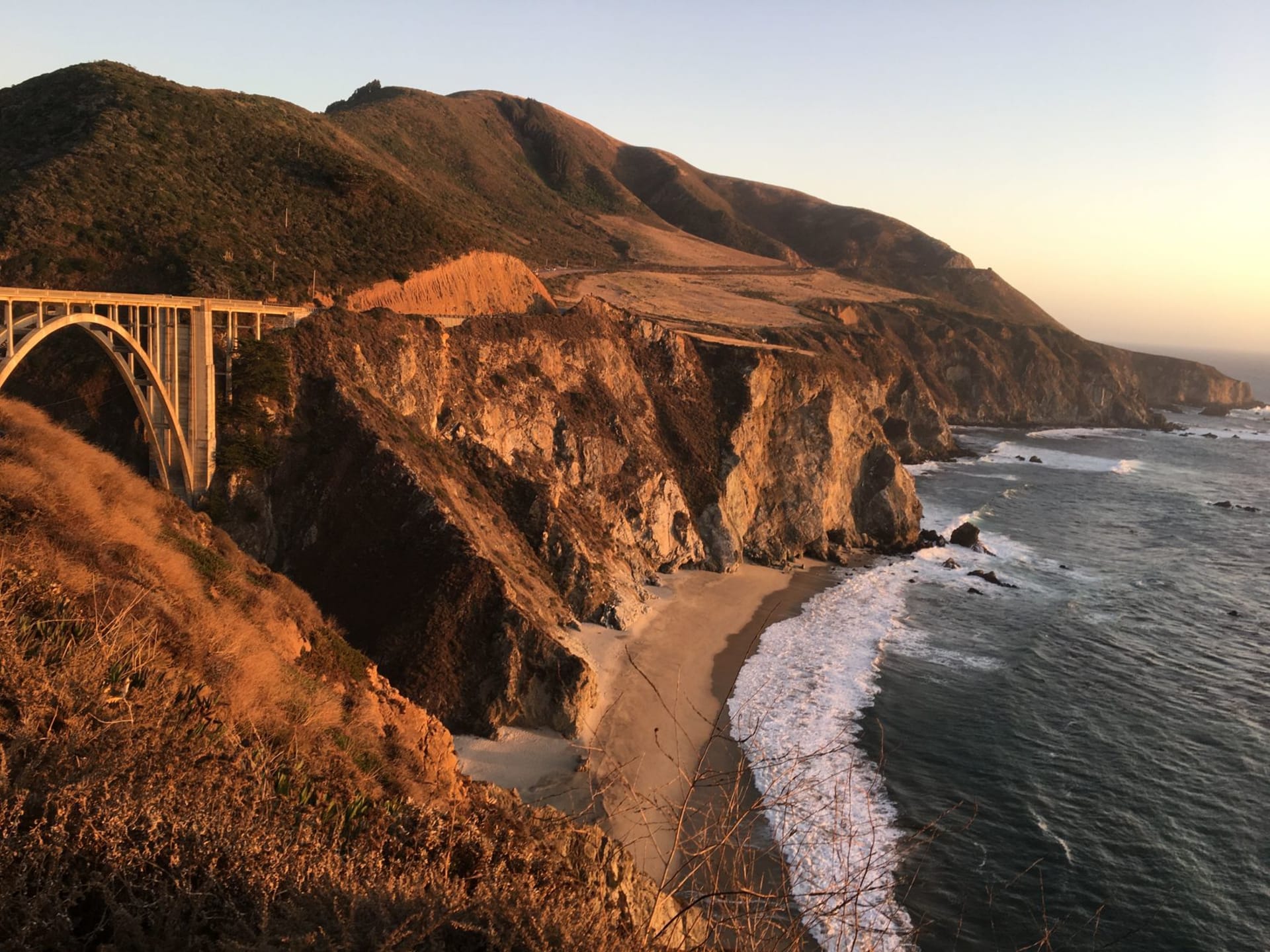 Bixby Creek Bridge arching over the Big Sur coastline at dramatic sunset, orange light on rugged cliffs above the Pacific