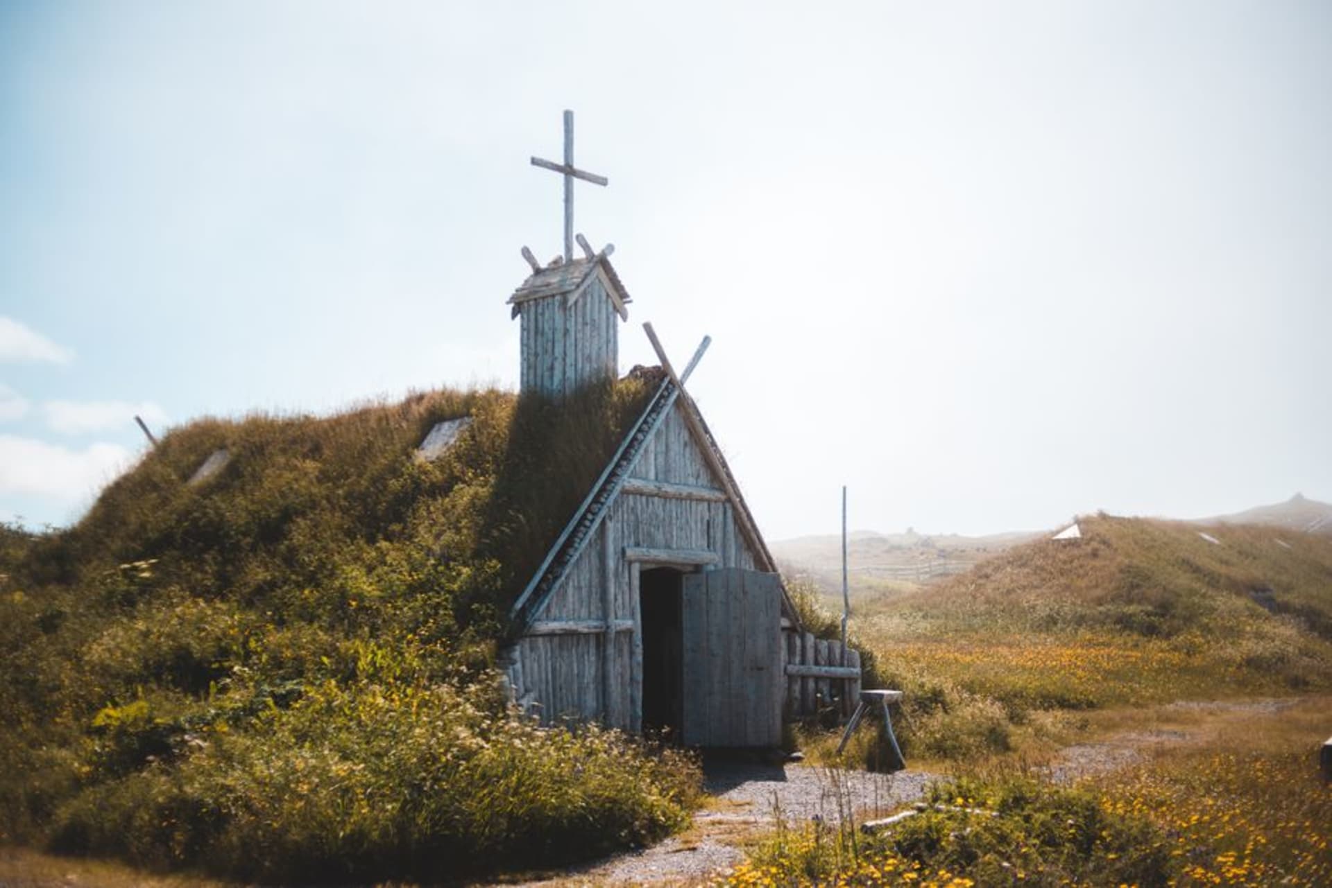 Reconstructed Norse sod longhouses on a green coastal meadow under a wide grey Newfoundland sky