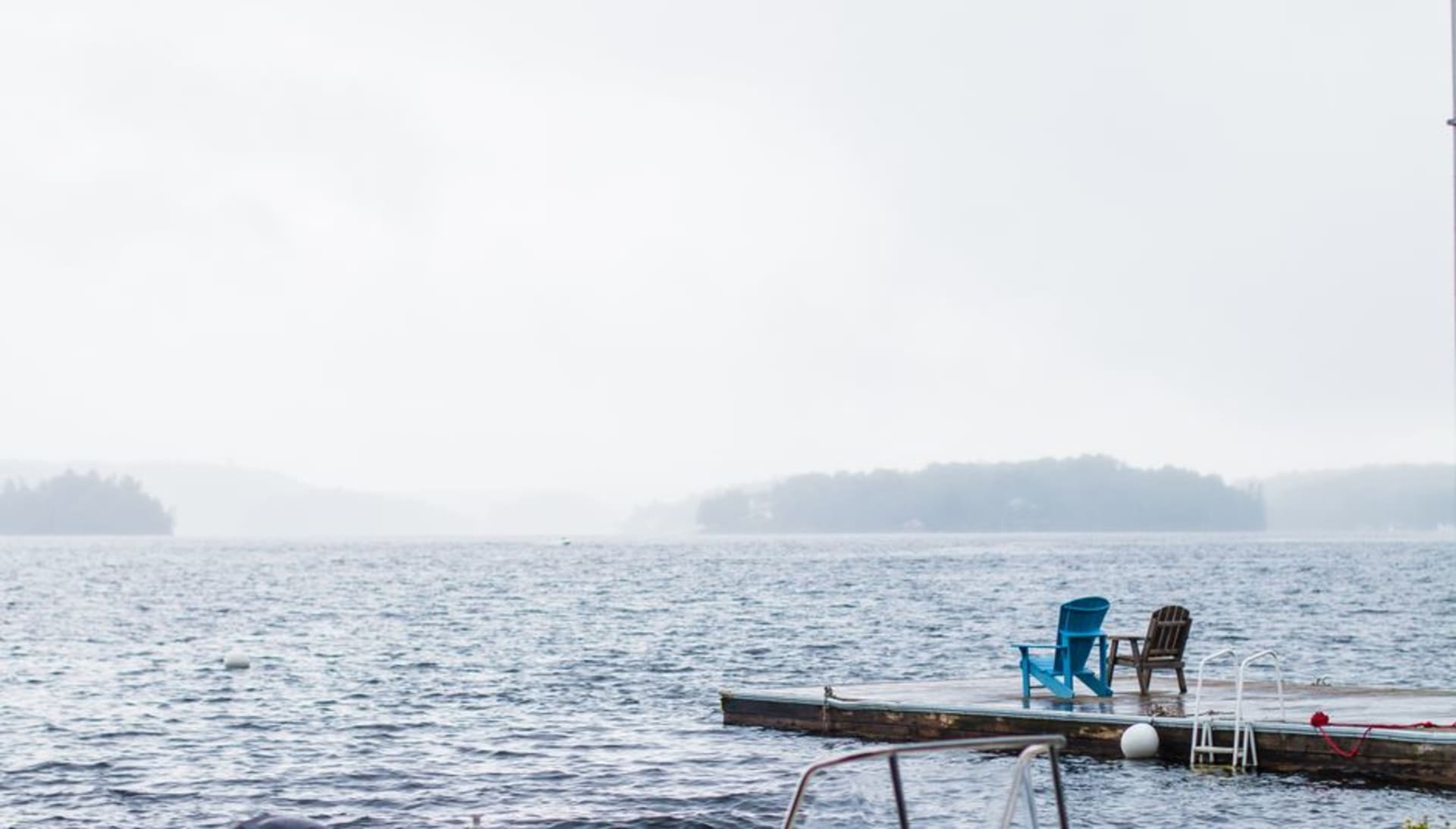 Row of colourful wooden Muskoka chairs facing a calm lake at sunset with pine trees along the shore