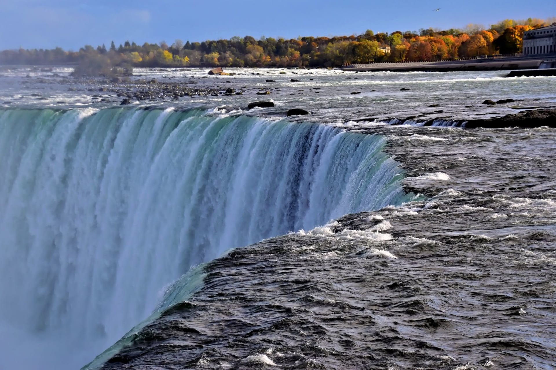 The curved green crest of the Horseshoe Falls thundering over the edge into a cloud of mist, seen from the Canadian side at Niagara.