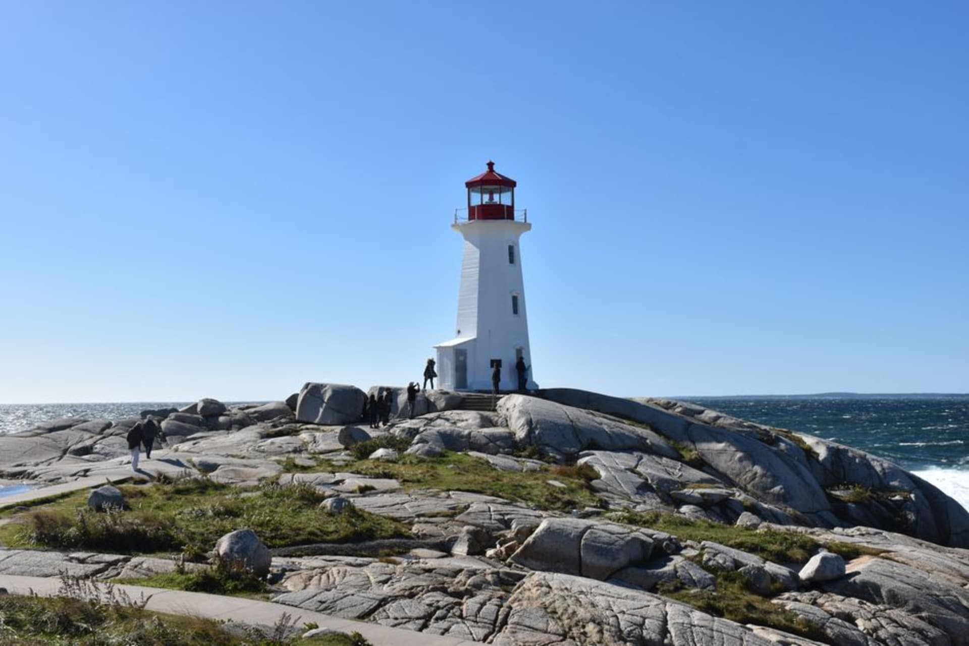 Red and white Peggy's Cove lighthouse standing on smooth wave-worn granite rocks