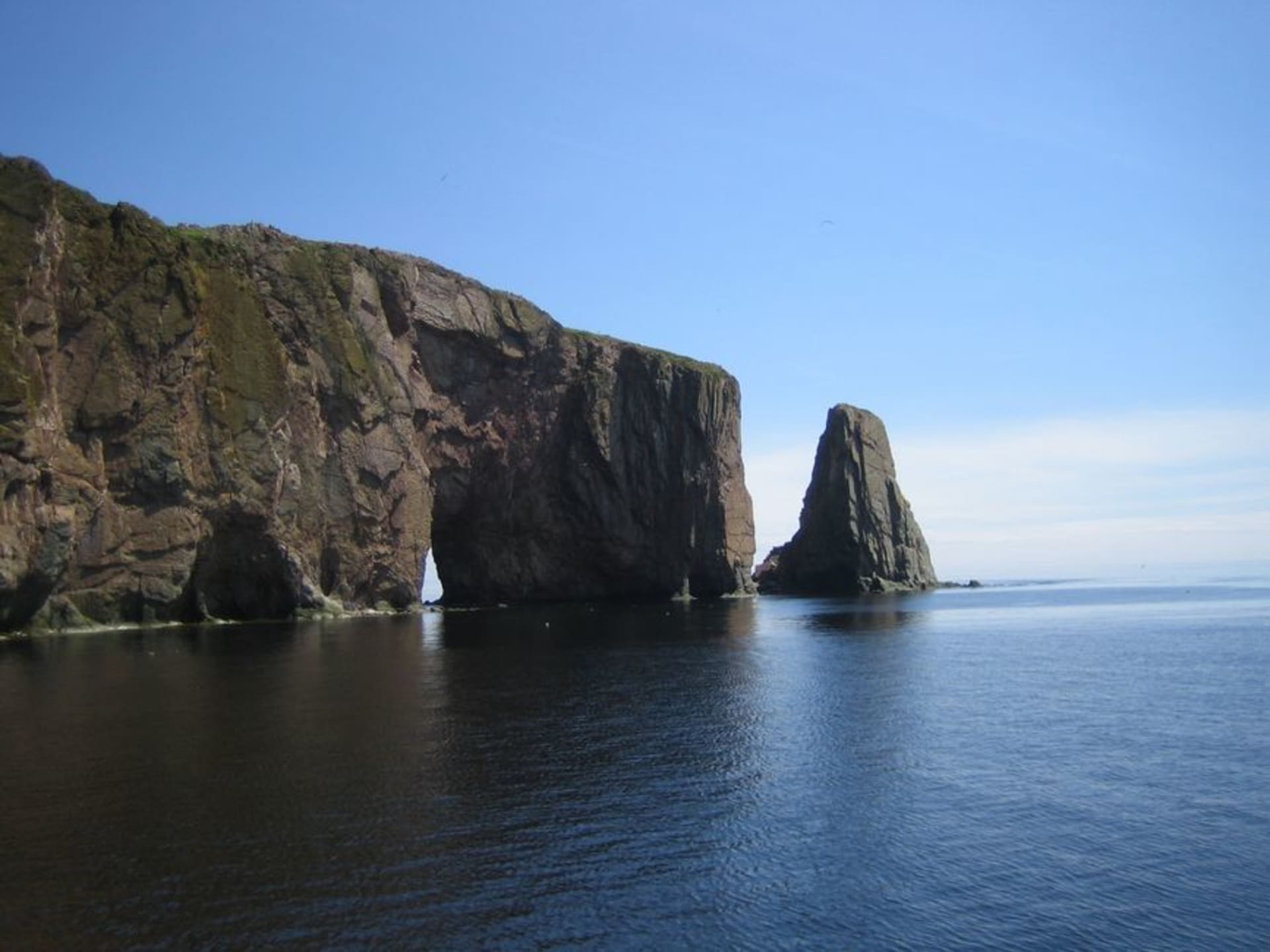 Percé Rock, a massive offshore limestone formation with a natural arch, seen from the village shore