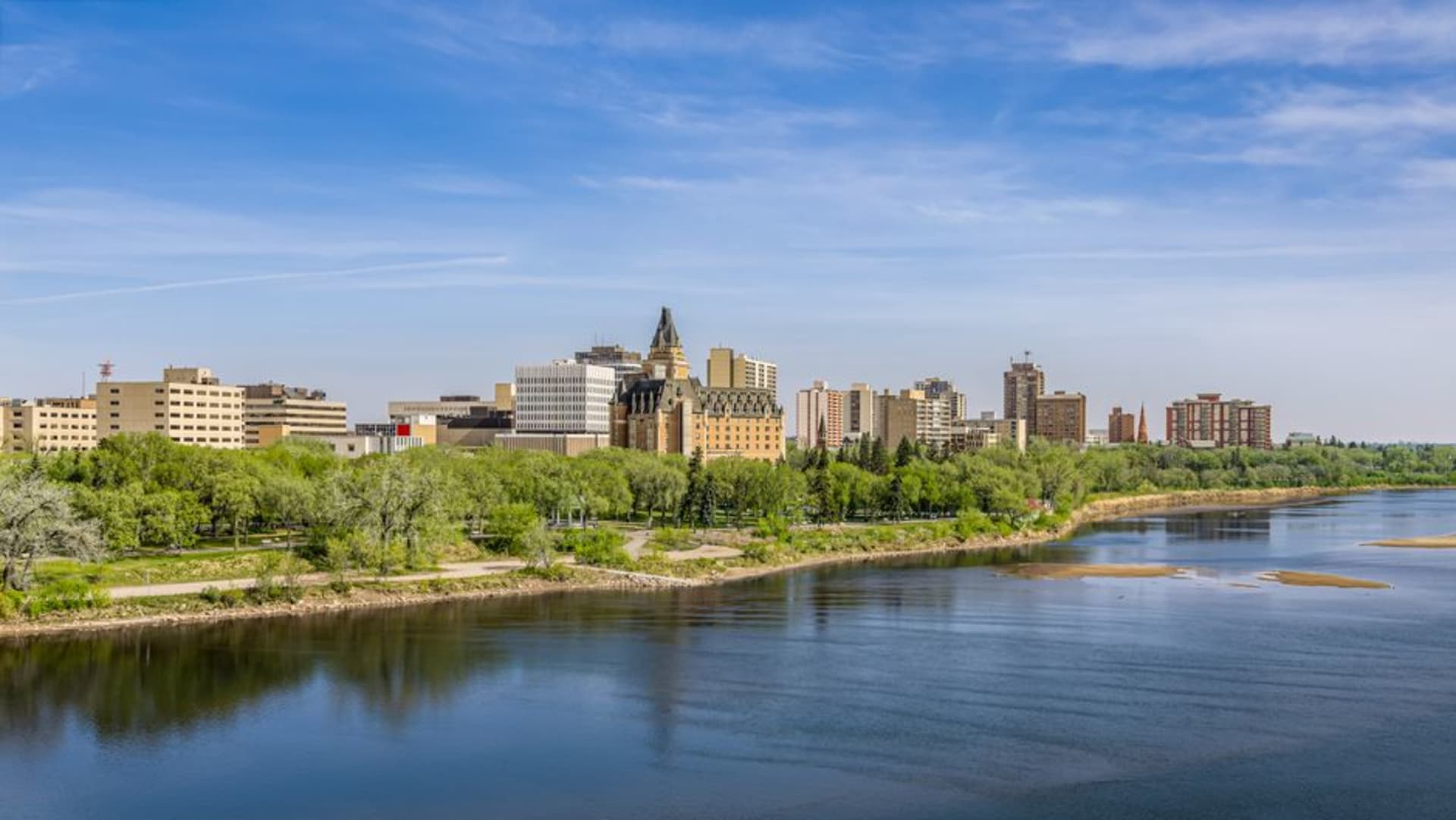 Sweeping curve of the South Saskatchewan River lined with green riverbank trails through downtown Saskatoon