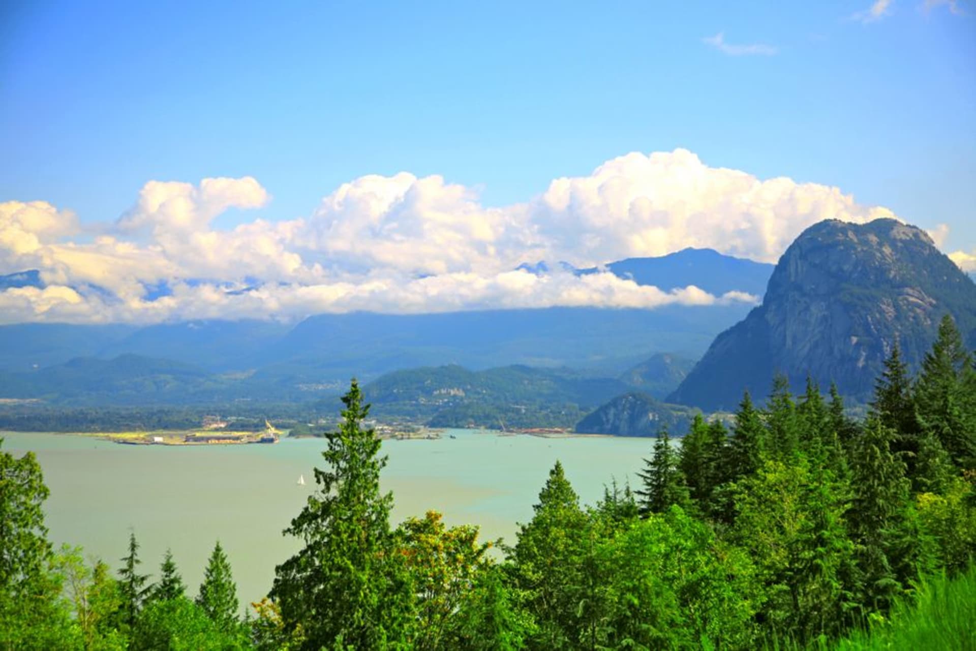 Highway 99 curving along a cliffside above the deep blue waters of Howe Sound with forested mountains rising on both sides