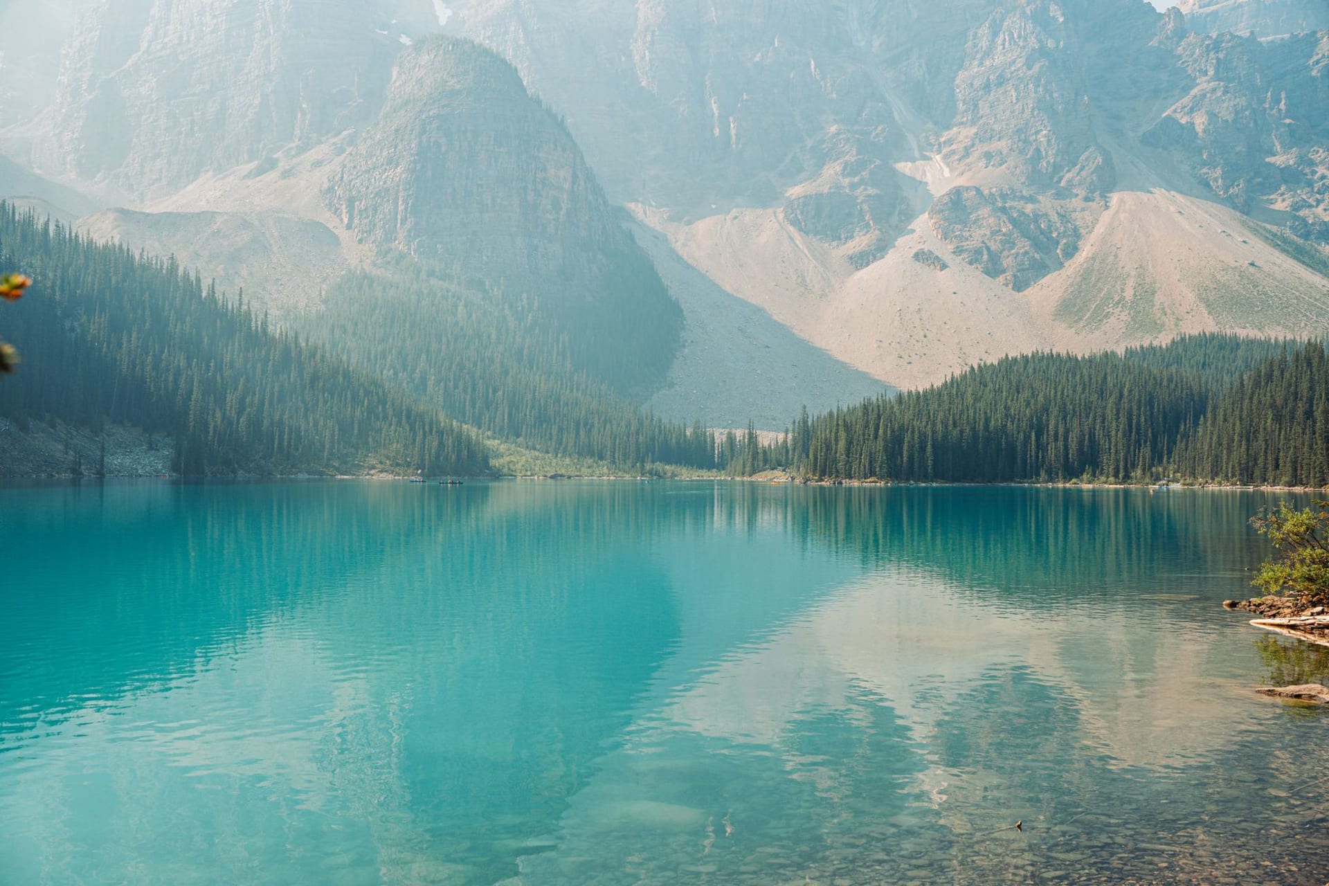 Turquoise mountain lake reflecting jagged snow-capped Rocky Mountain peaks under a partly cloudy sky