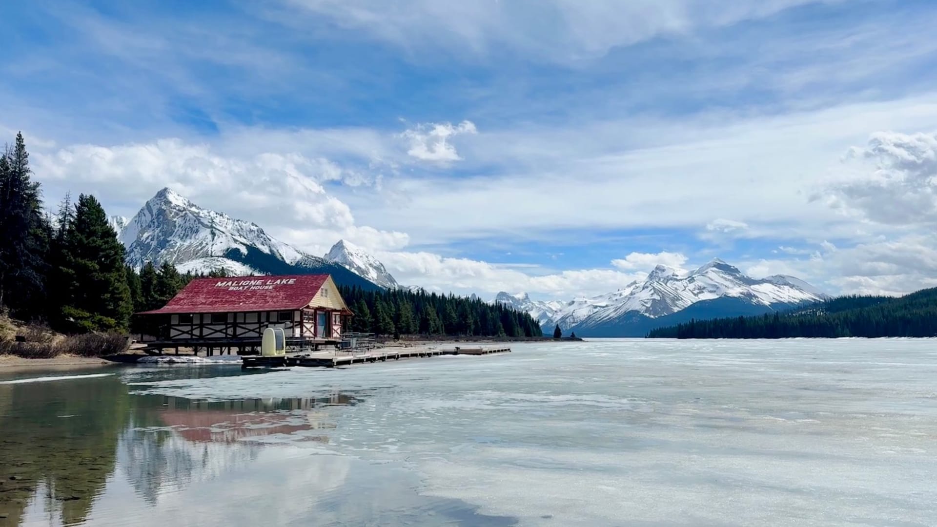 Spirit Island on Maligne Lake at golden hour, tiny in a vast expanse of jade water with snow-streaked peaks behind