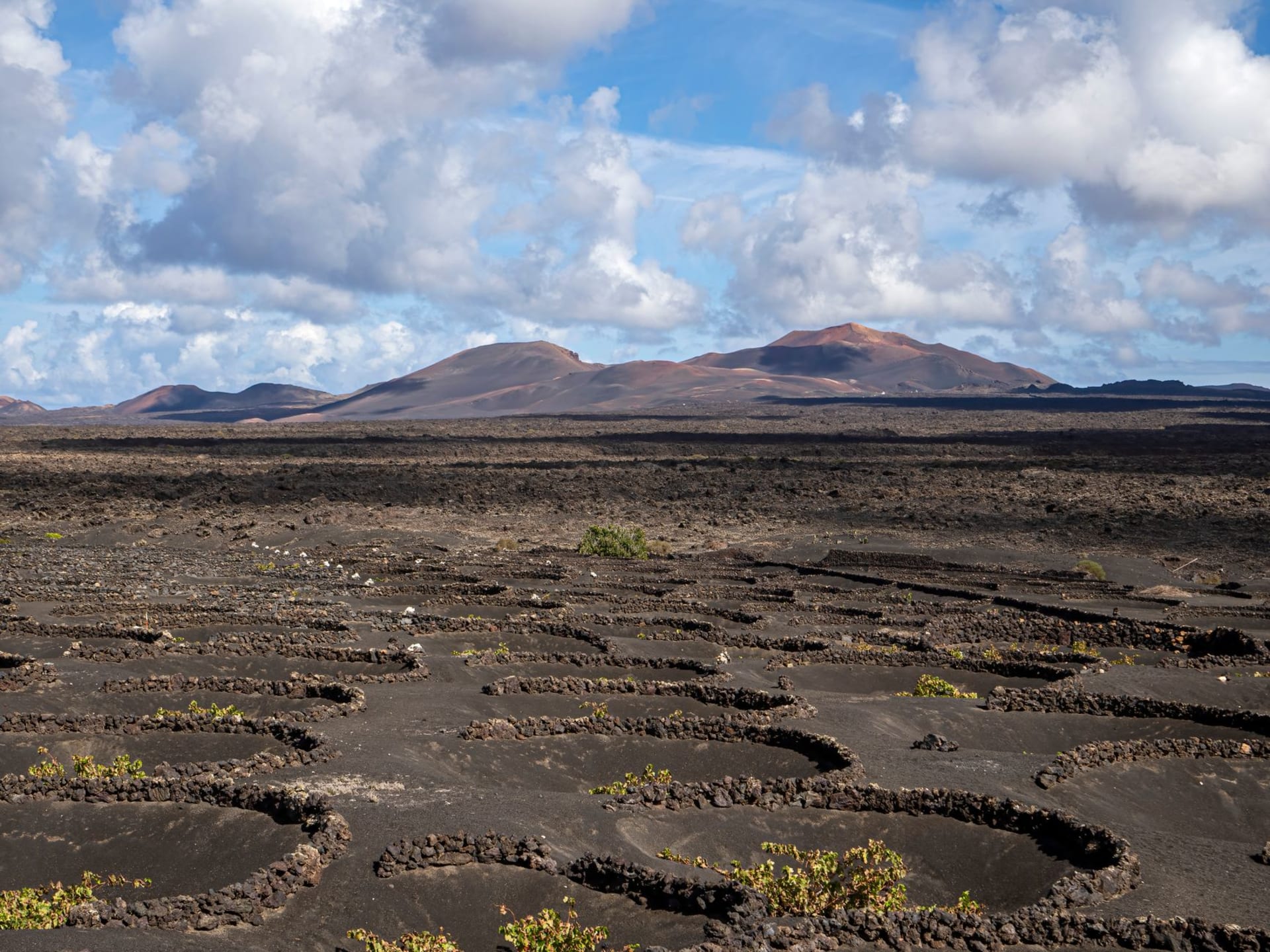 Vast red and black lava fields of Timanfaya with the fire mountains rising in the distance under a clear blue sky, Lanzarote