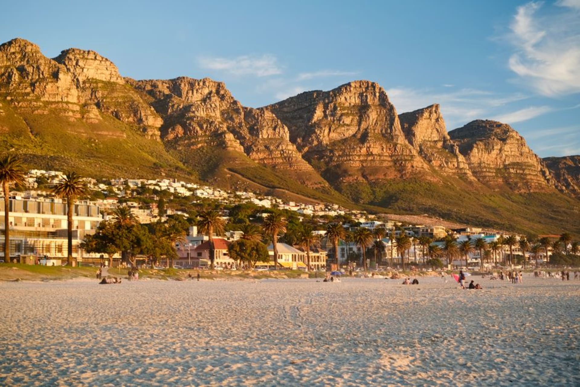 La playa de arena blanca de Camps Bay con la cordillera Twelve Apostles alzándose detrás de Victoria Road bordeada de palmeras