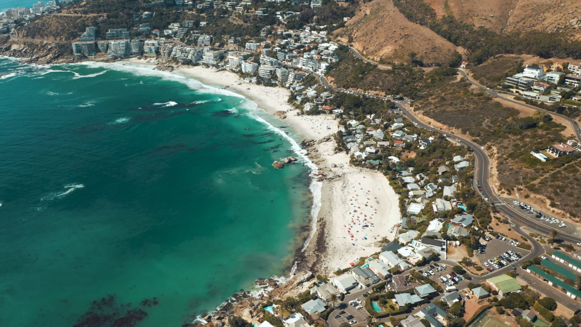Llandudno beach on the Cape Peninsula, a crescent of white sand framed by huge rounded granite boulders, with mountains rising steeply behind under golden evening light