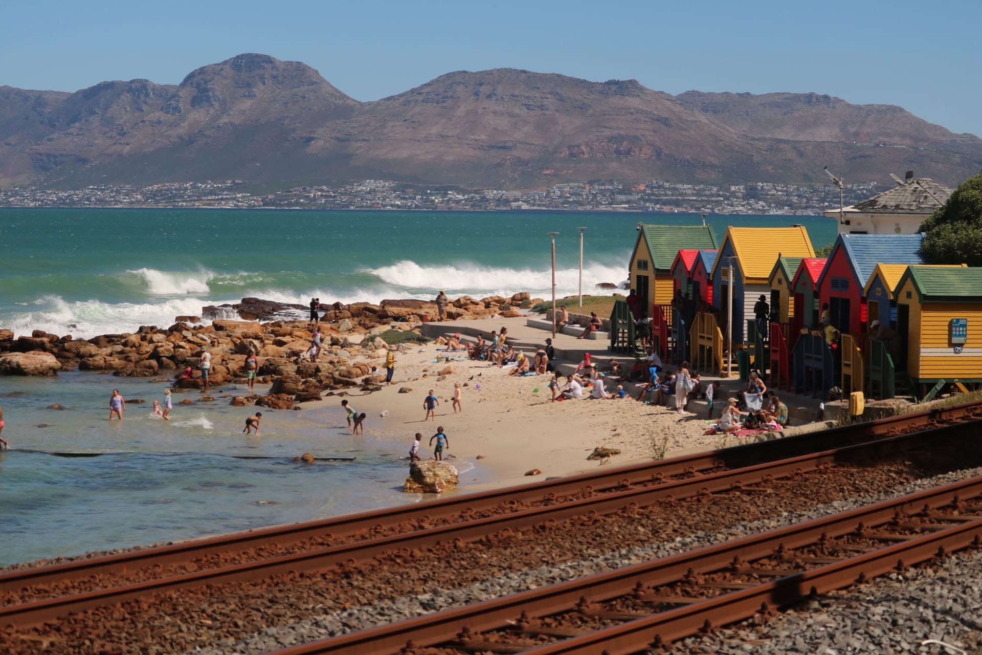 Muizenberg's row of brightly striped Victorian bathing boxes on the beach with learner surfers in the small breaking waves