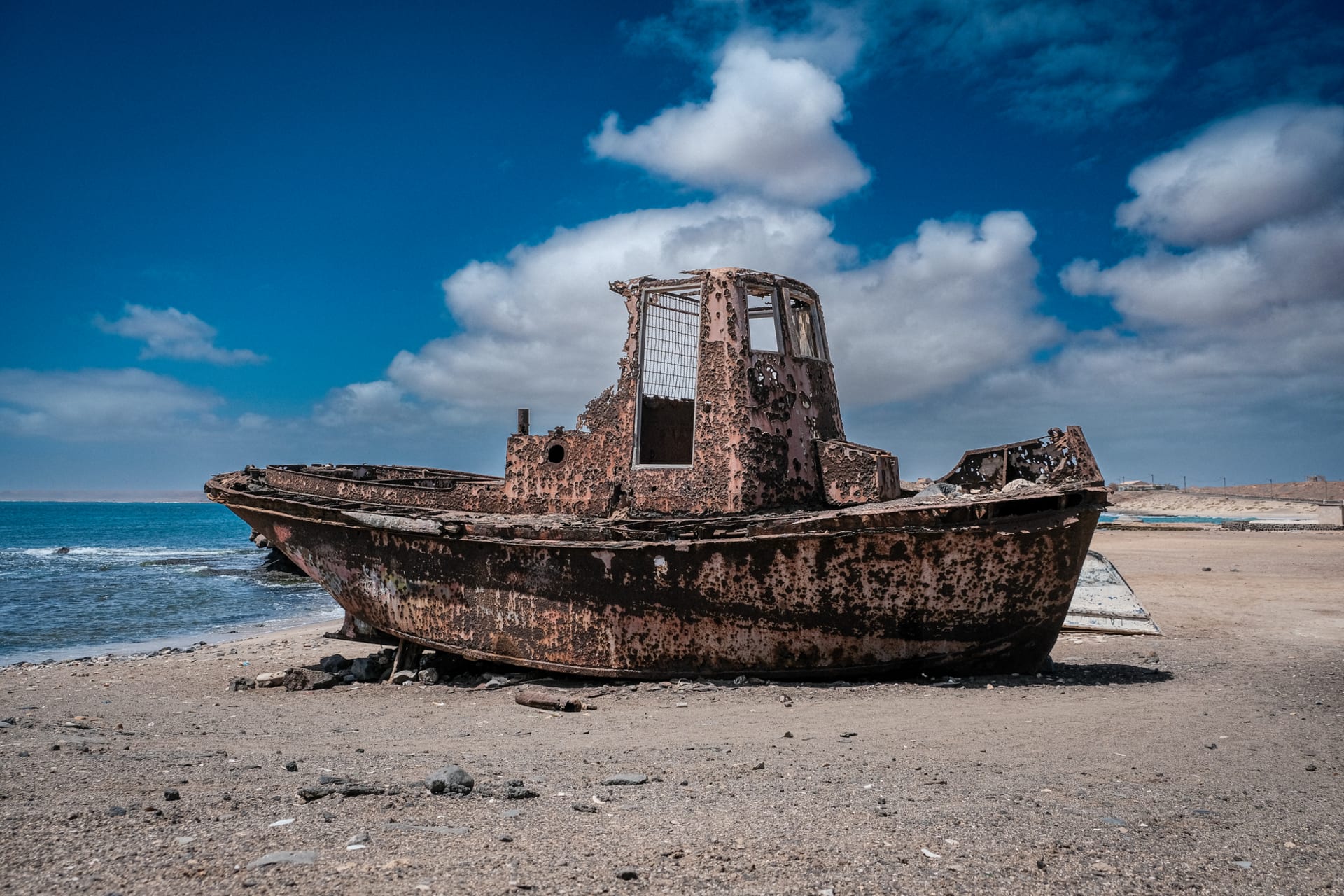 An abandoned rusty boat resting on the sandy shores of Pedra Lume salt crater, Sal Island, under a vivid blue Atlantic sky