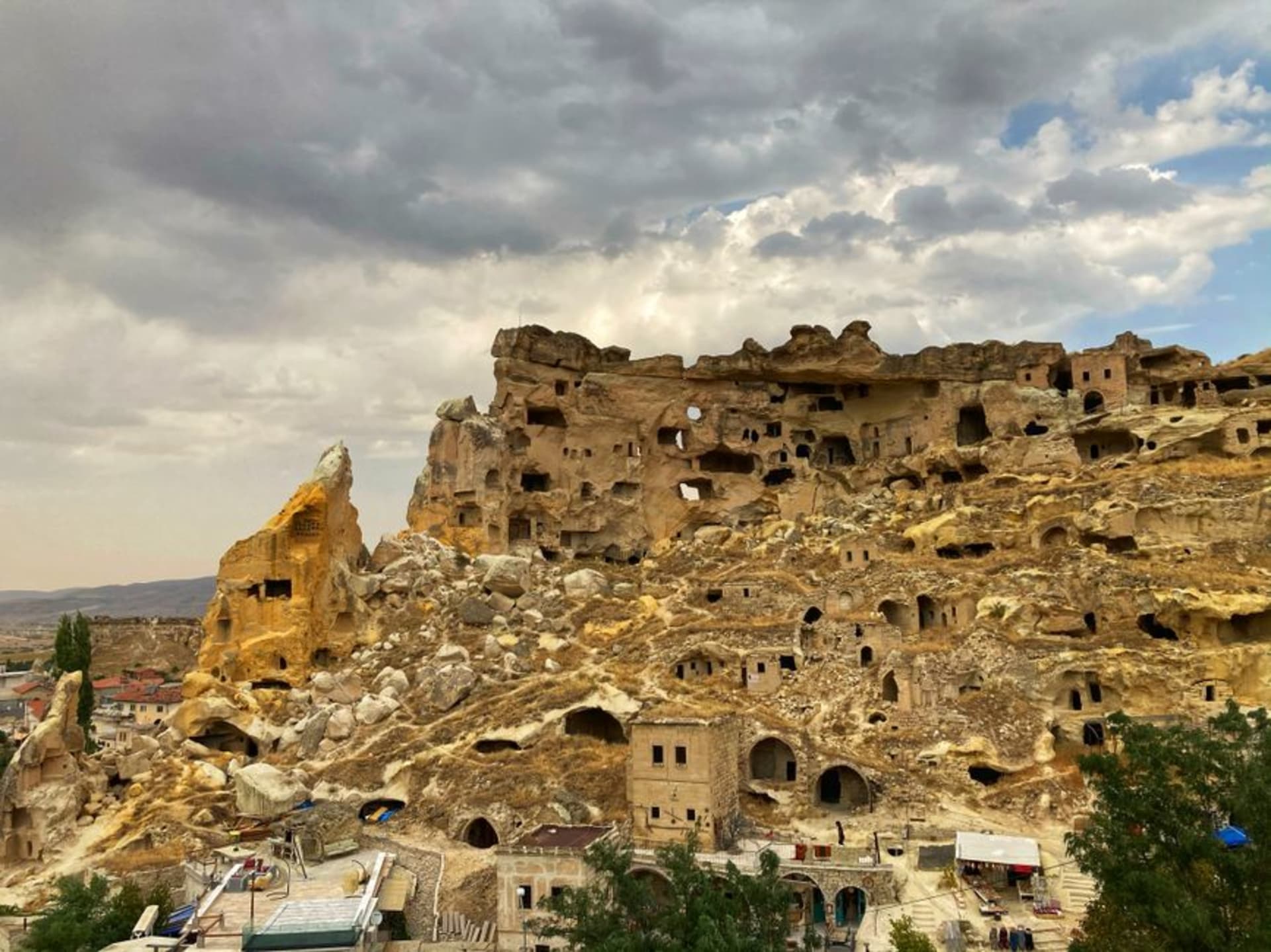 La cara del acantilado del antiguo pueblo de Çavuşin, lleno de viviendas rupestres abandonadas, elevándose sobre el pueblo moderno y la carretera