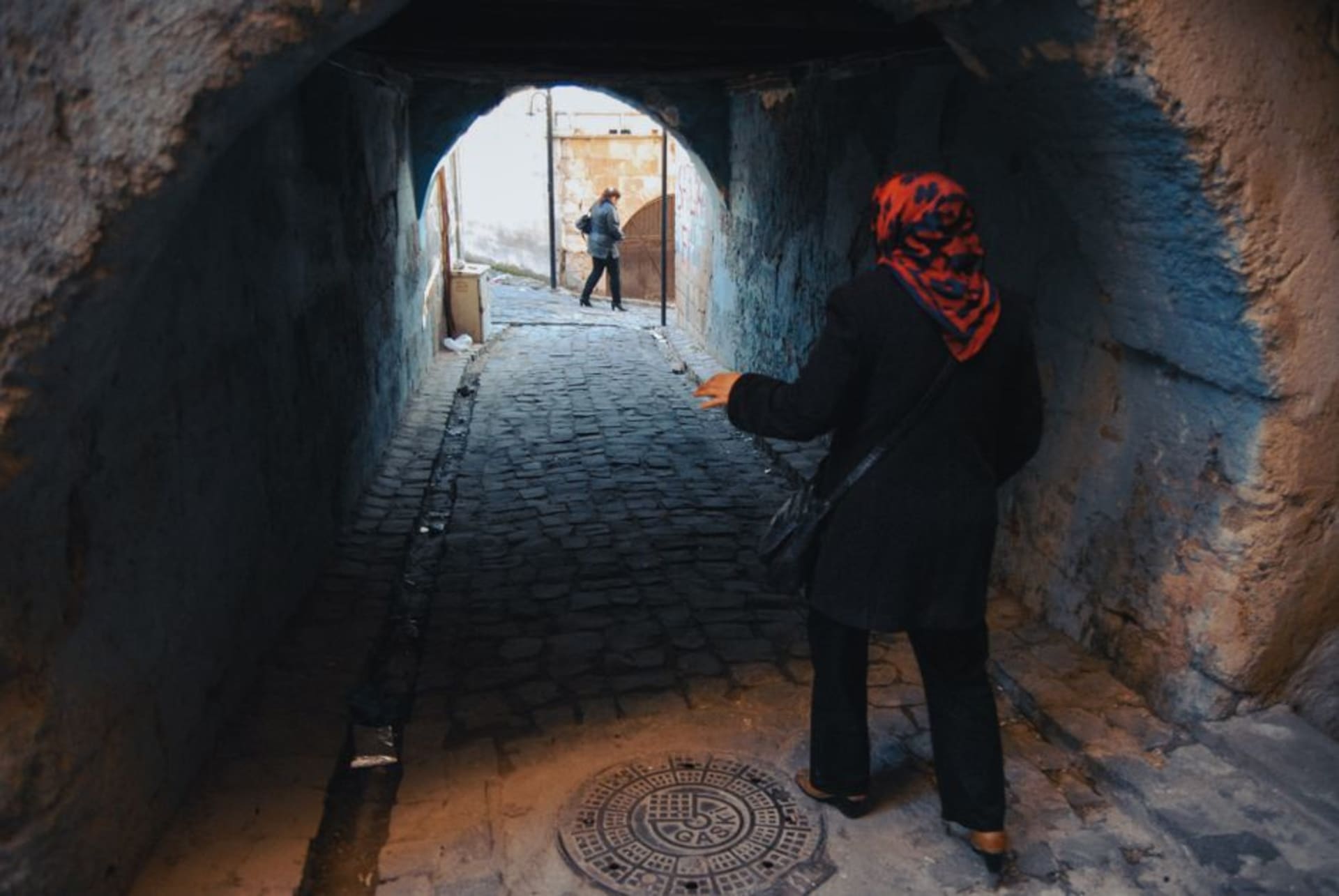 A narrow carved tunnel descending into the Özkonak underground city, lit by a single bulb strung along the passage