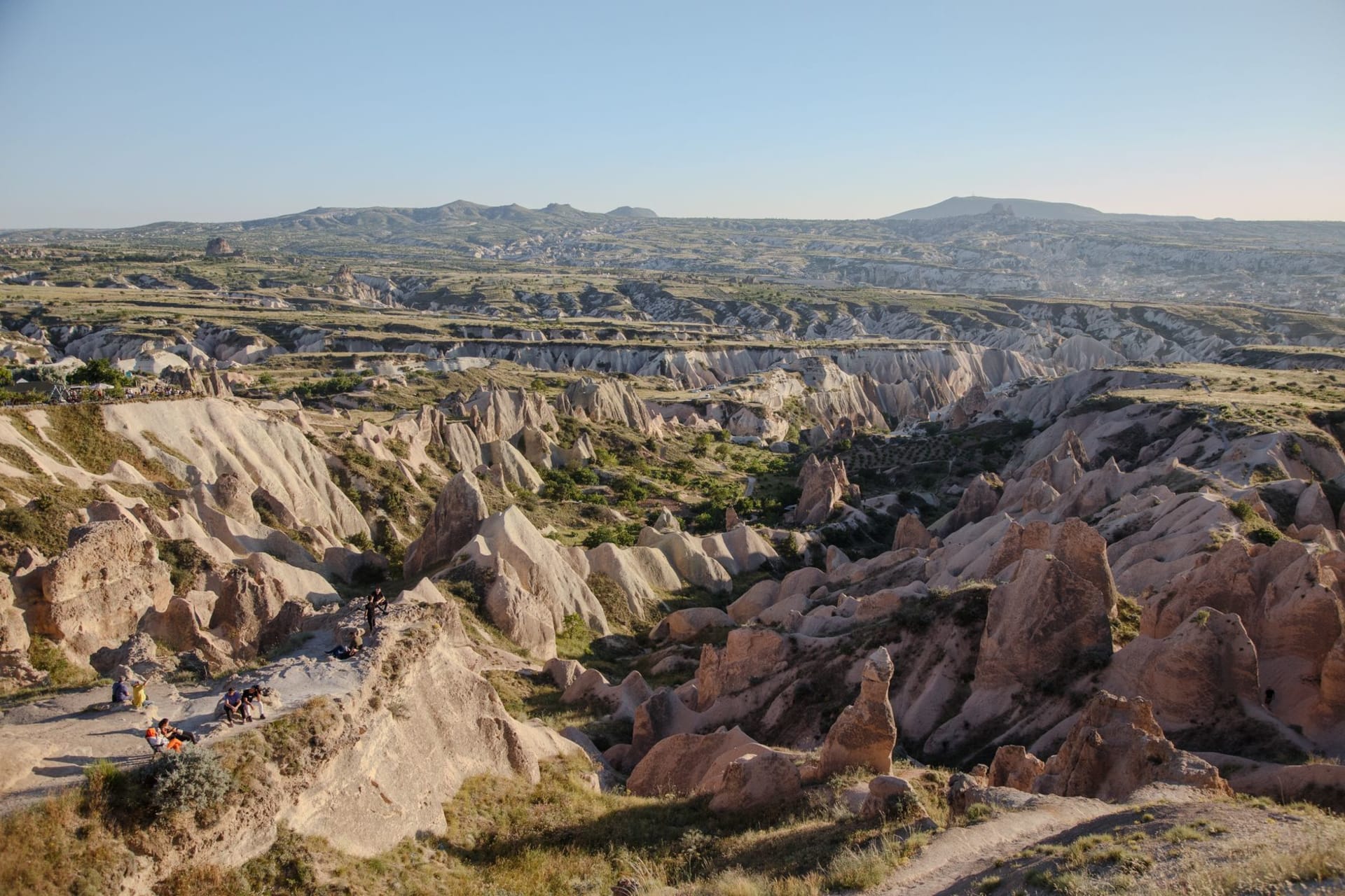 The Rose Valley's pinkish-red tufa formations glowing deep at sunset, cave-church openings carved into the warm-toned cliffs