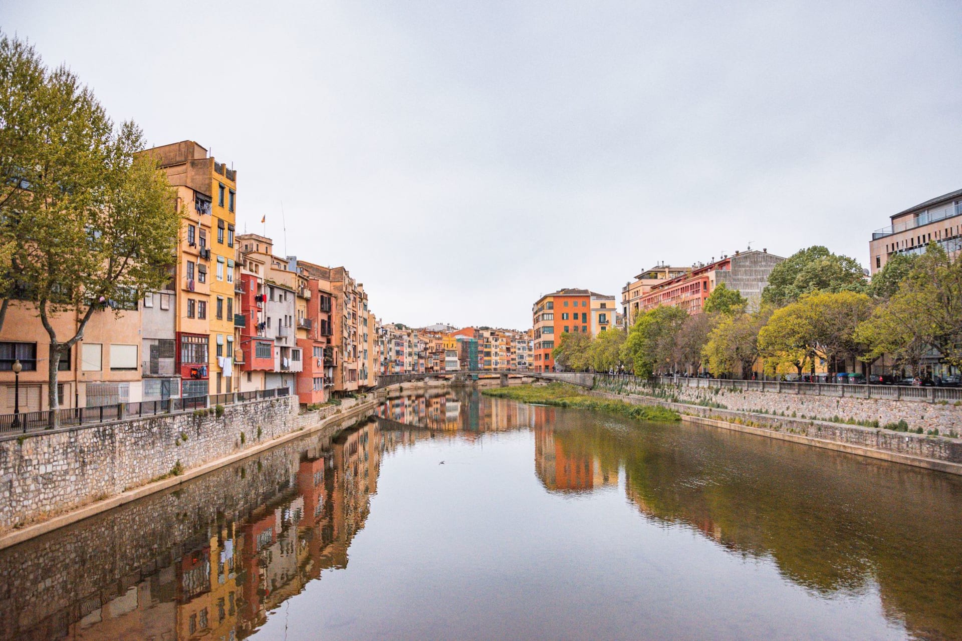 The colorful houses of the Onyar river in Girona reflected in the still water, with cathedral towers above