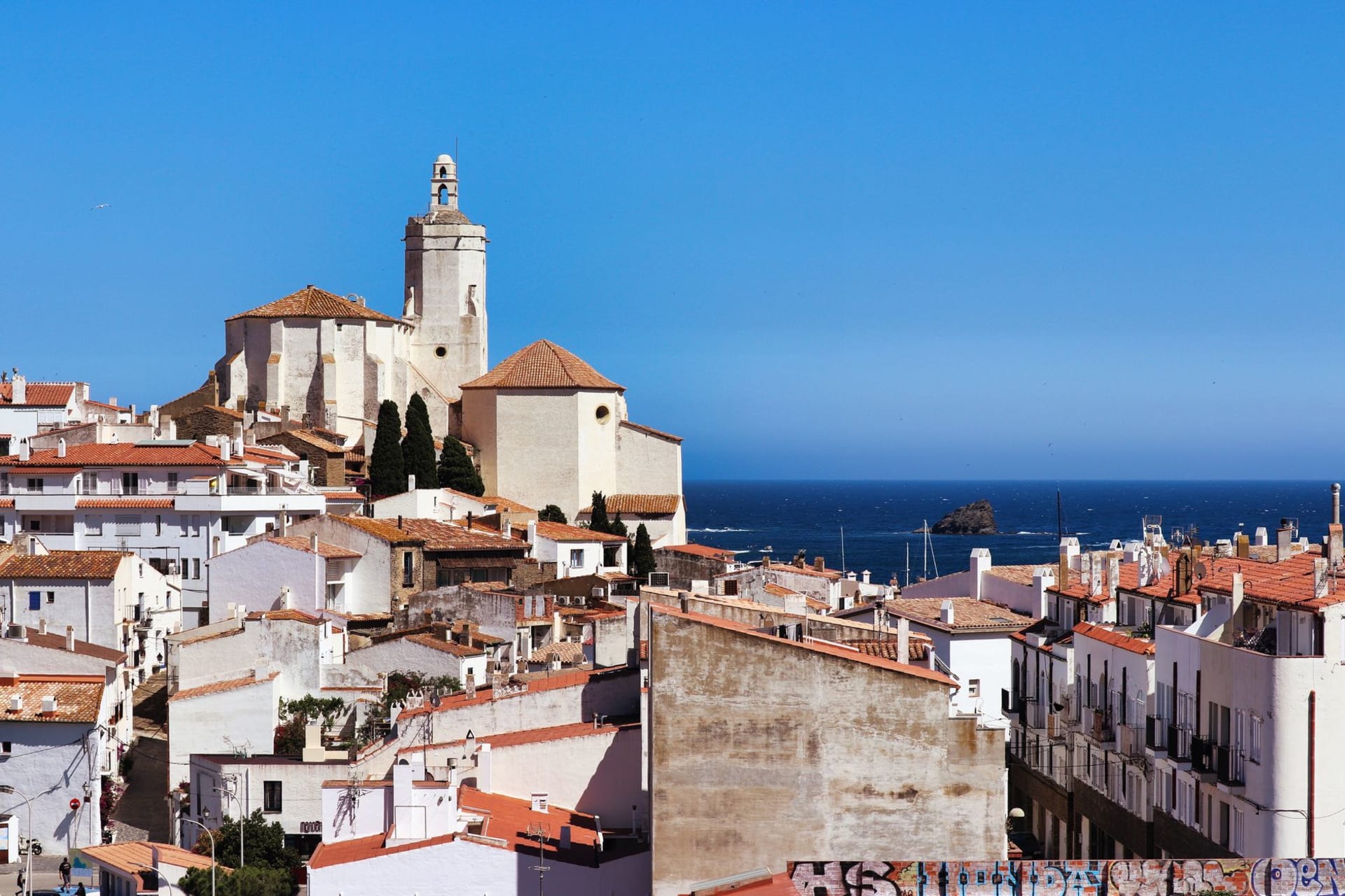 The church of Sant Bartomeu i Santa Tecla in Sitges standing on a rocky outcrop above the Mediterranean, whitewashed old town houses and a sandy beach beside it