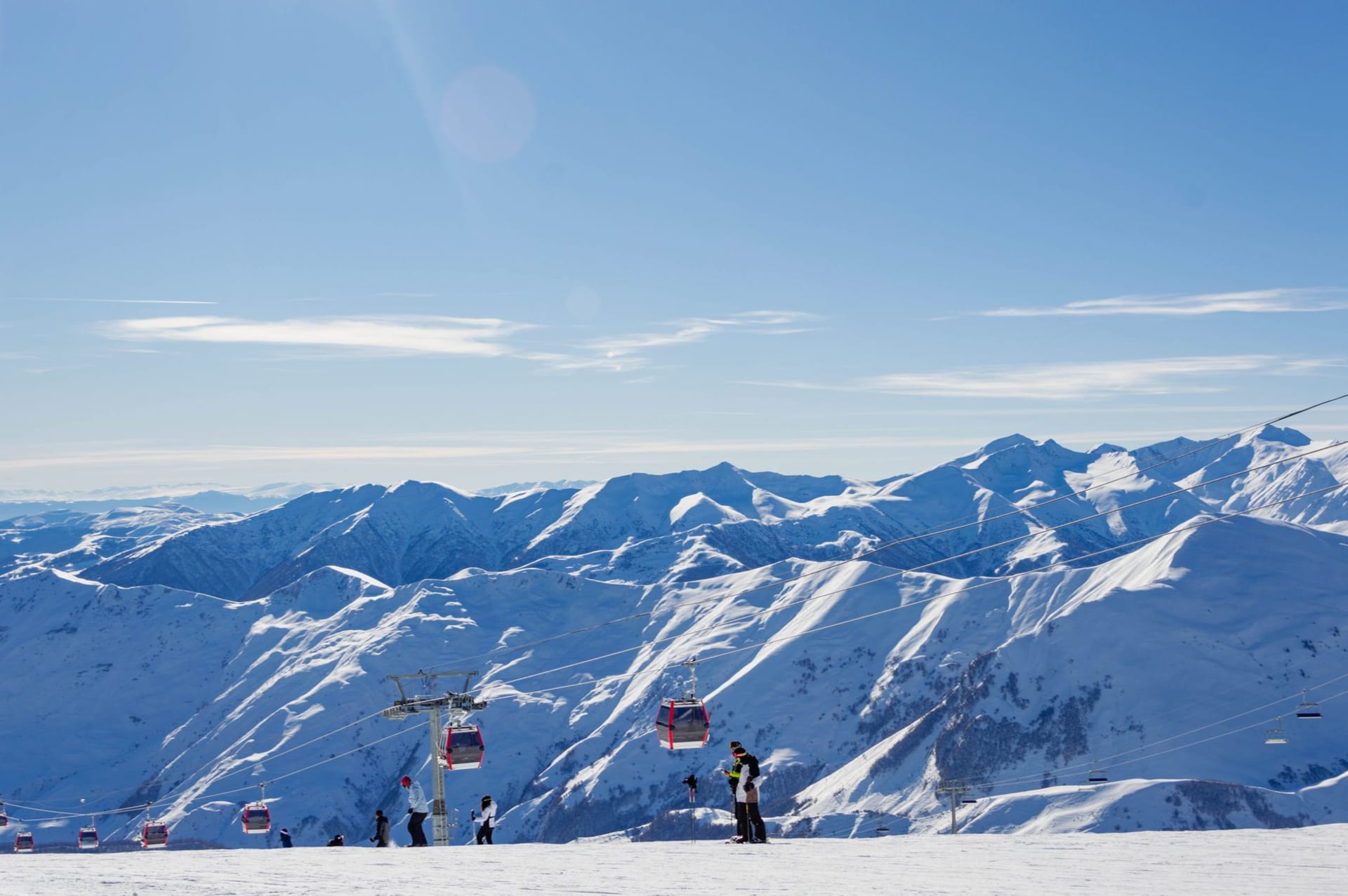 Paraglider launching from the Gudauri plateau edge above the deep Aragvi gorge, snow-capped Caucasus peaks spreading across the horizon behind