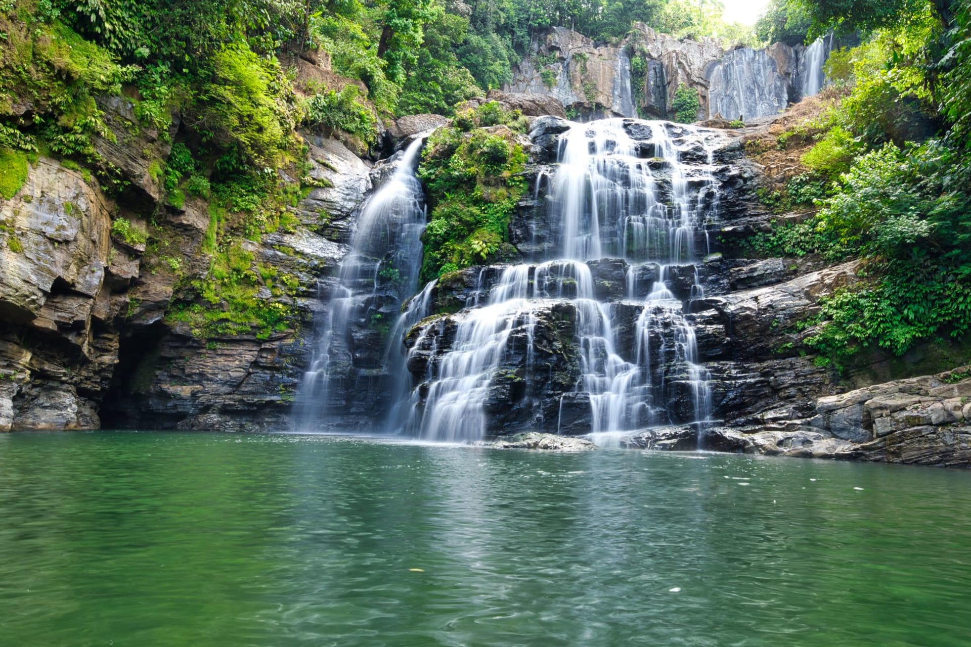 Boali waterfall cascading over dark basalt cliffs into a mist-filled gorge, surrounded by tropical vegetation in Central African Republic